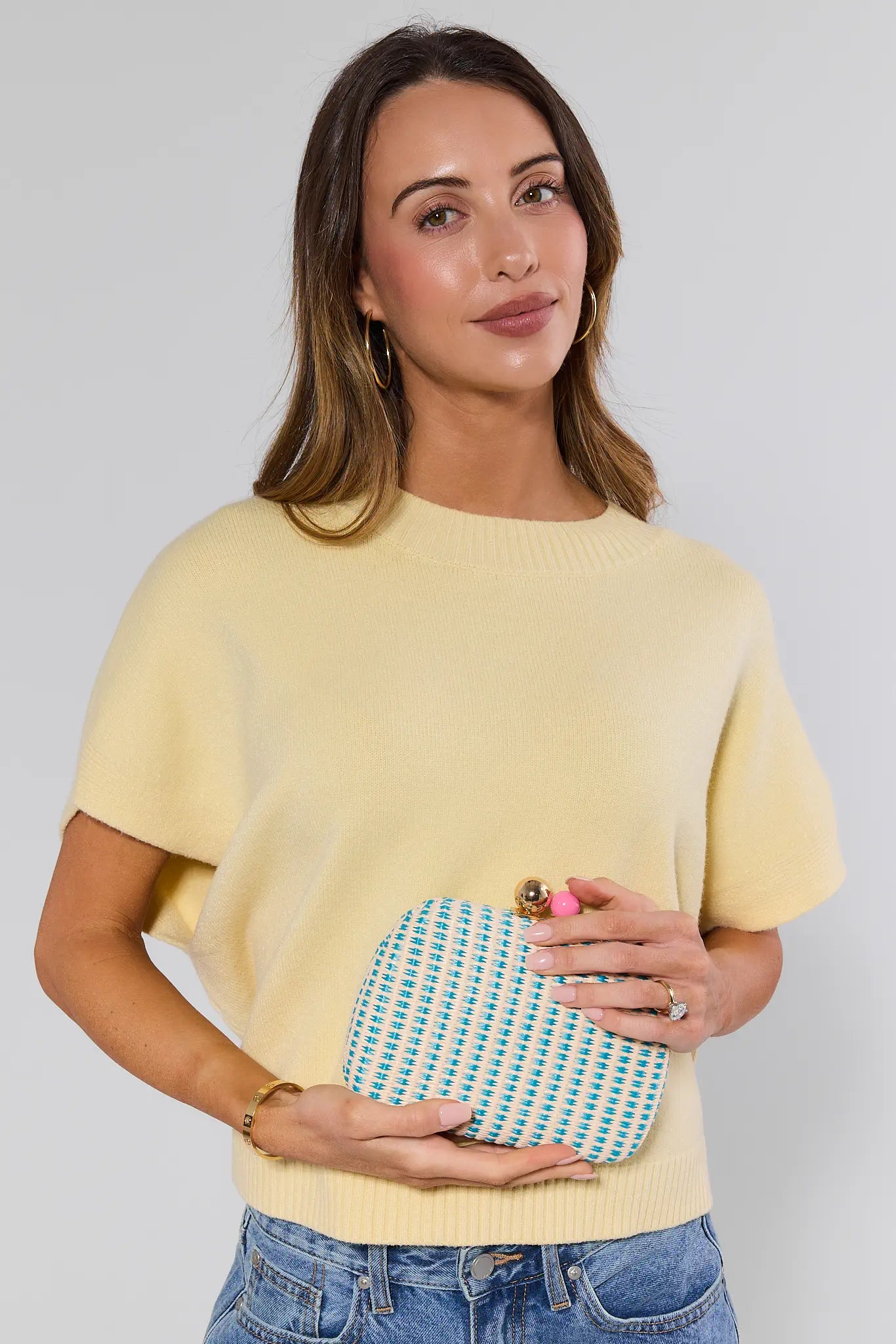 Woman holding a blue and white patterned clutch against a plain background
