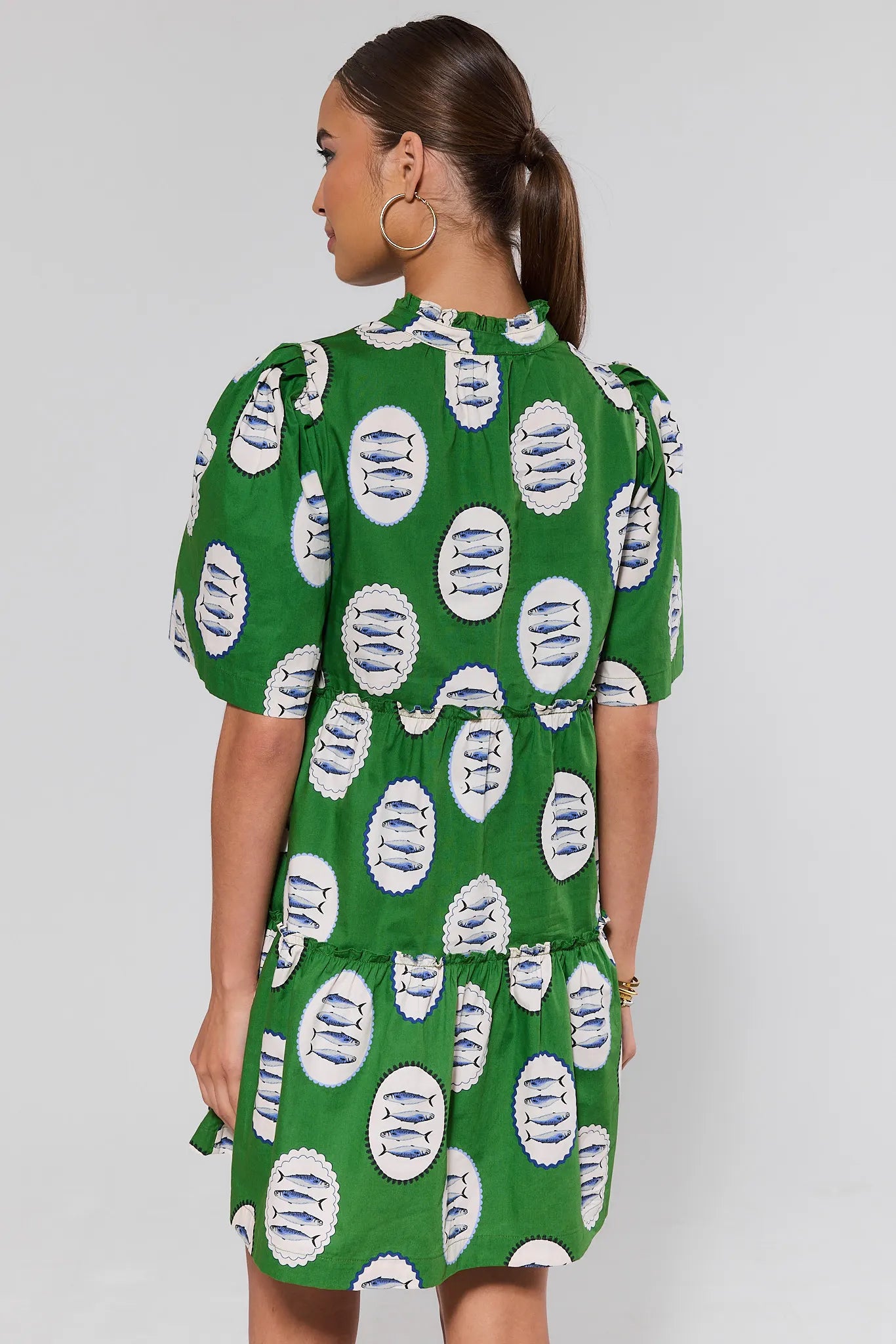 Woman standing wearing a green dress with white pattern on a plain background