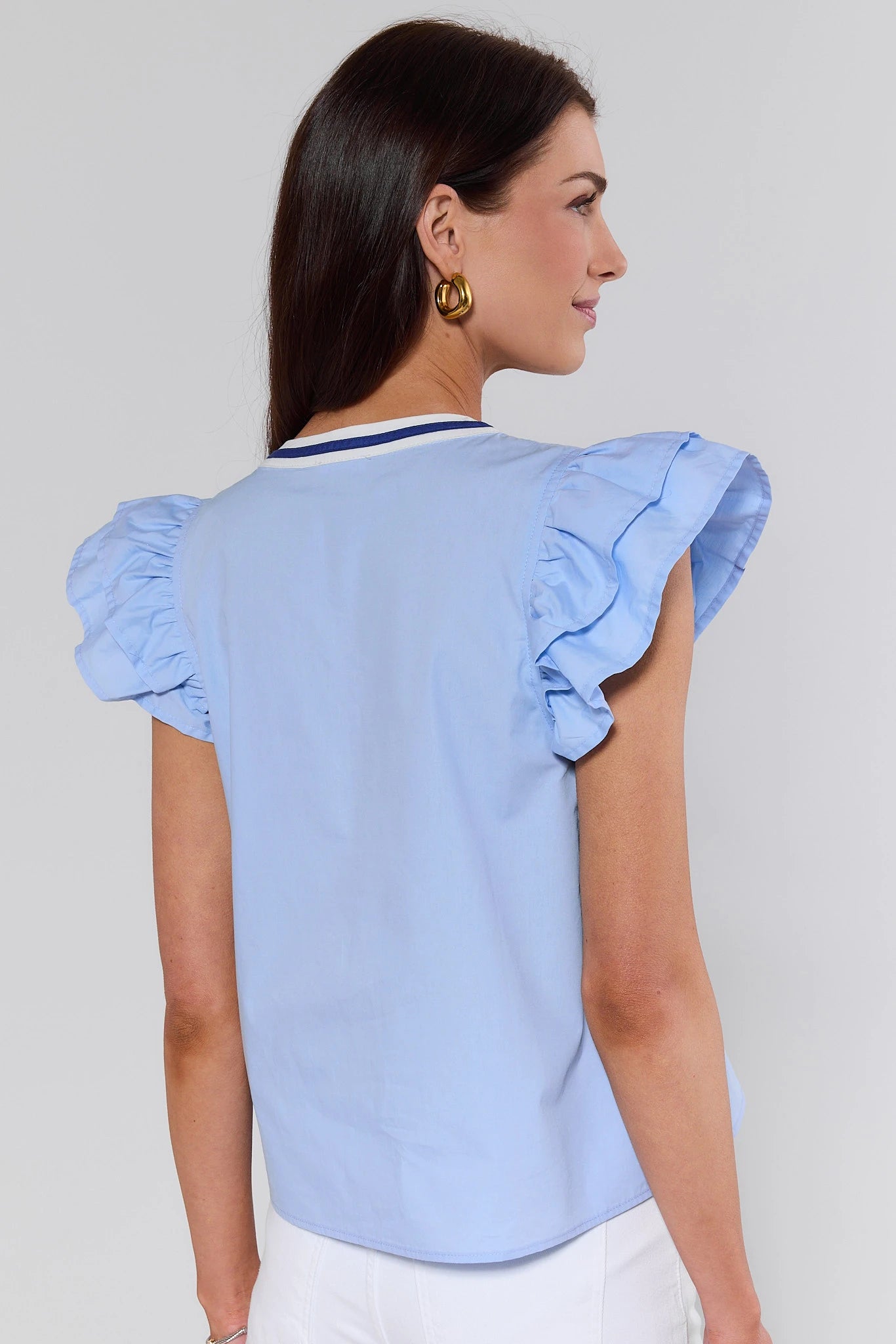 Woman standing wearing a light blue blouse with ruffled sleeves against a plain background