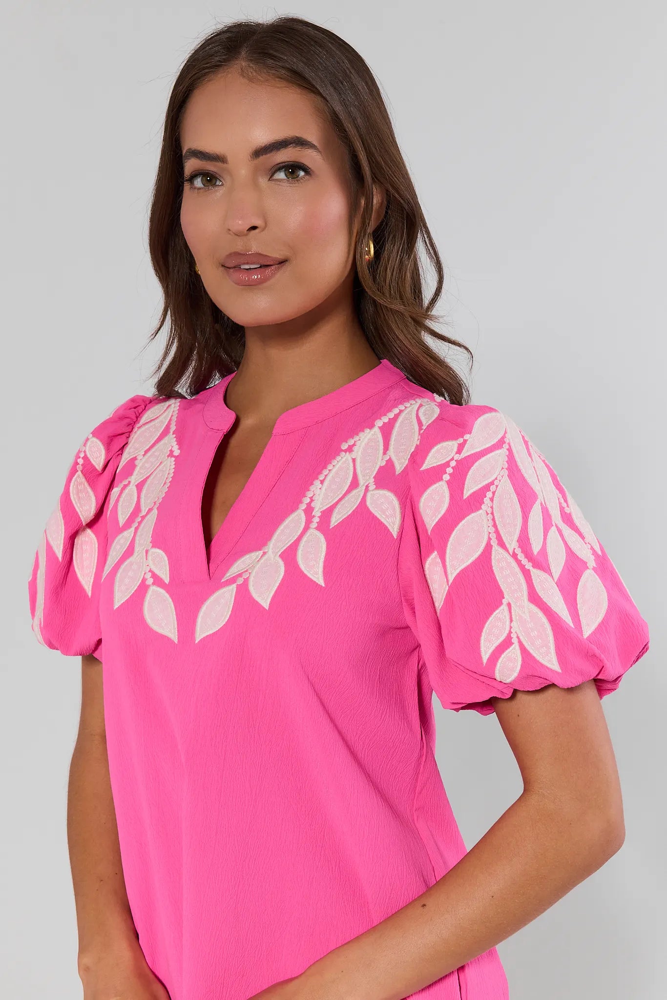 close up Woman wearing a pink blouse with white leaf patterns on a plain background