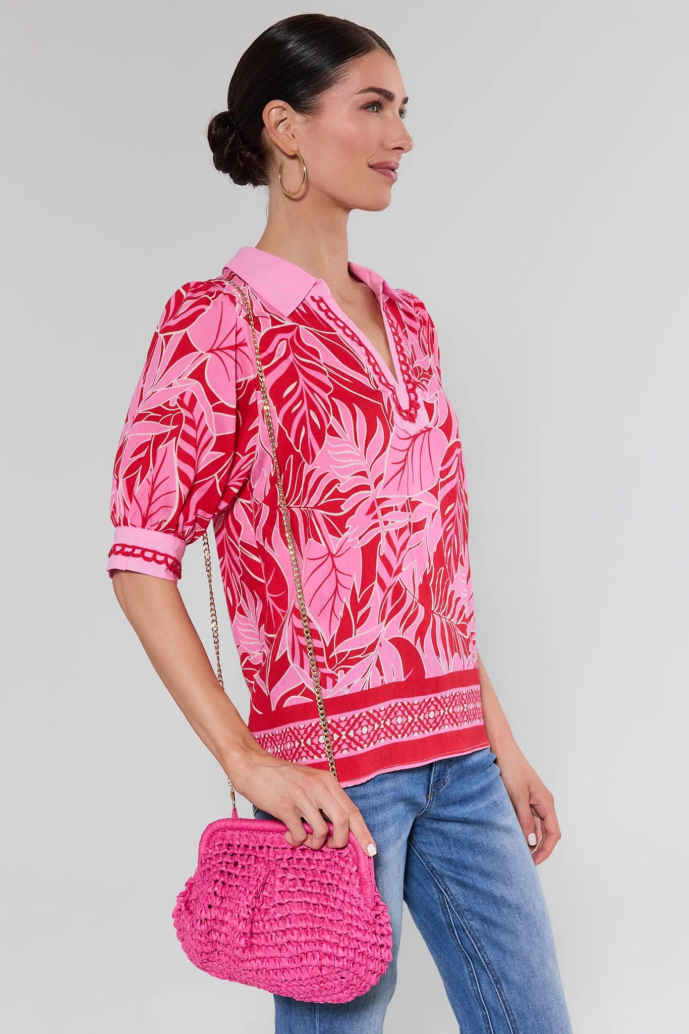 Woman wearing a pink patterned blouse and holding a pink handbag against a gray background