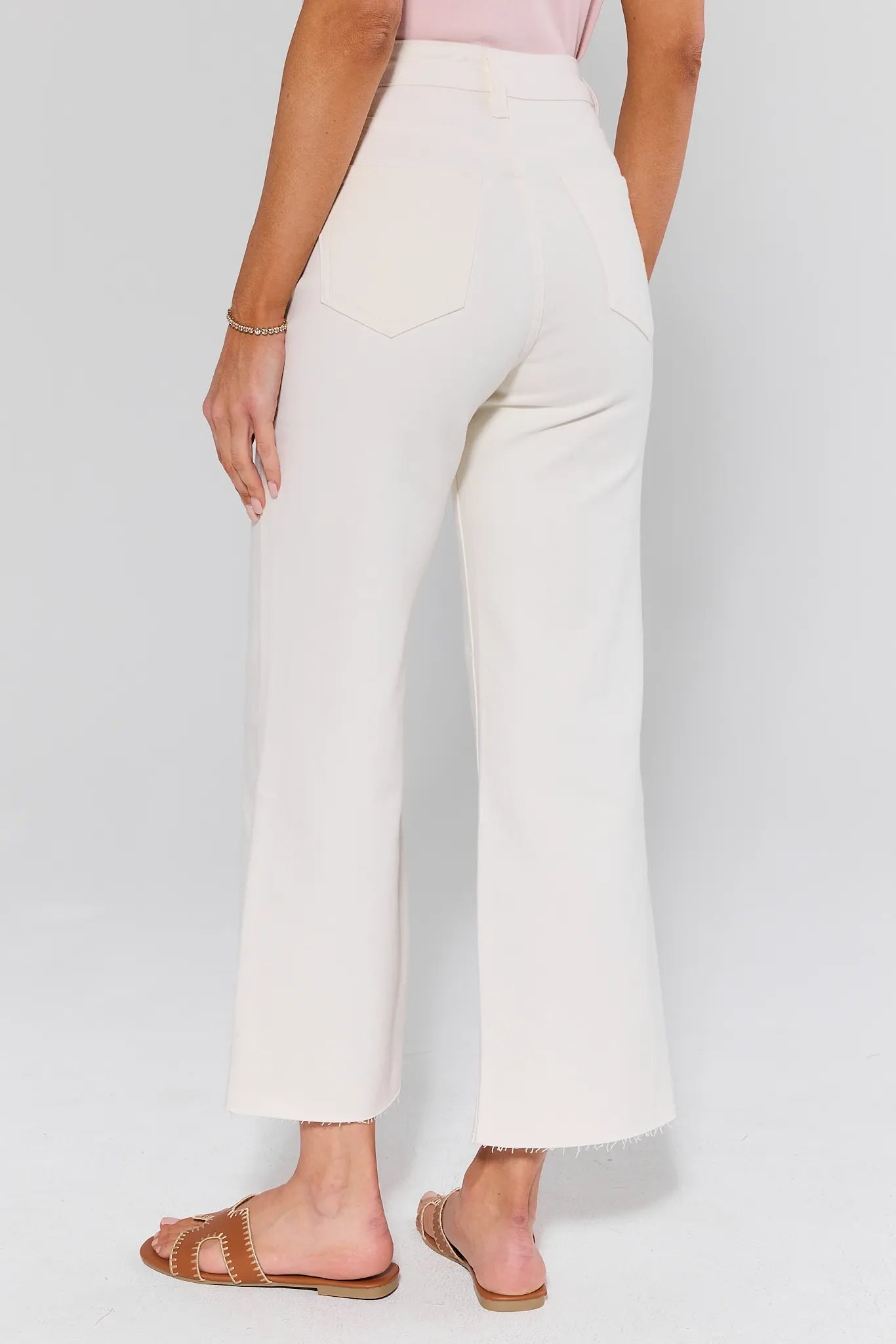 Caroline Ecru Straight Leg Jeans, high-waisted with a raw hem, are paired with tan slide sandals, showcasing a chic, cropped wide-leg style.