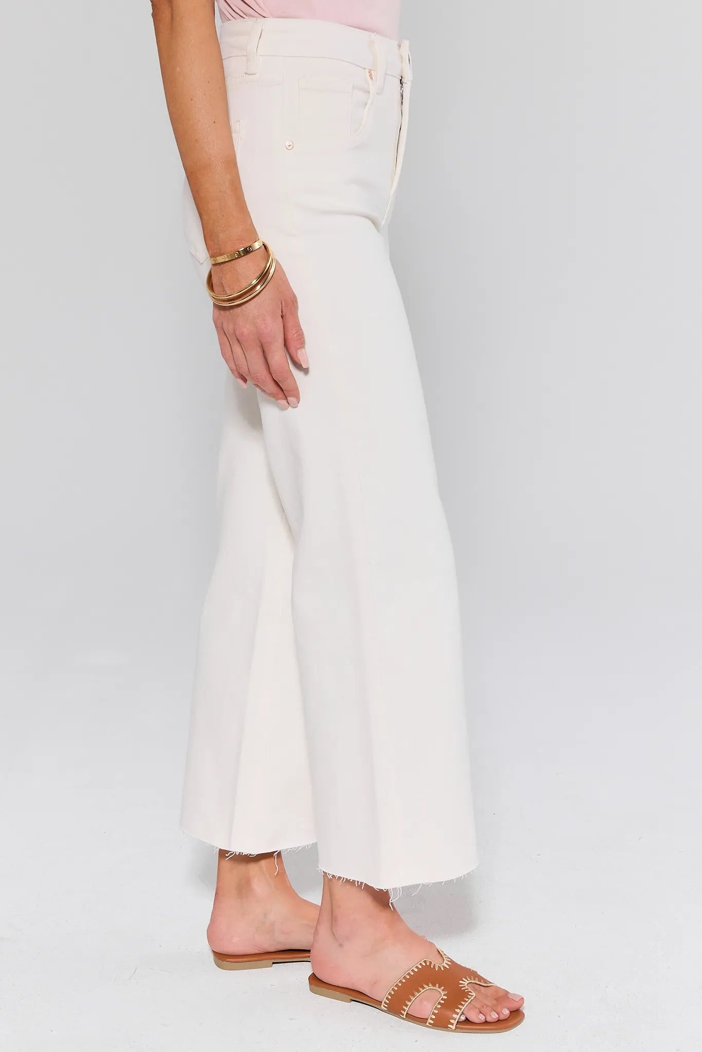 Caroline Ecru Straight Leg Jeans feature a high-waisted, wide-leg cropped design with raw hems, styled with tan slides and gold bangles.