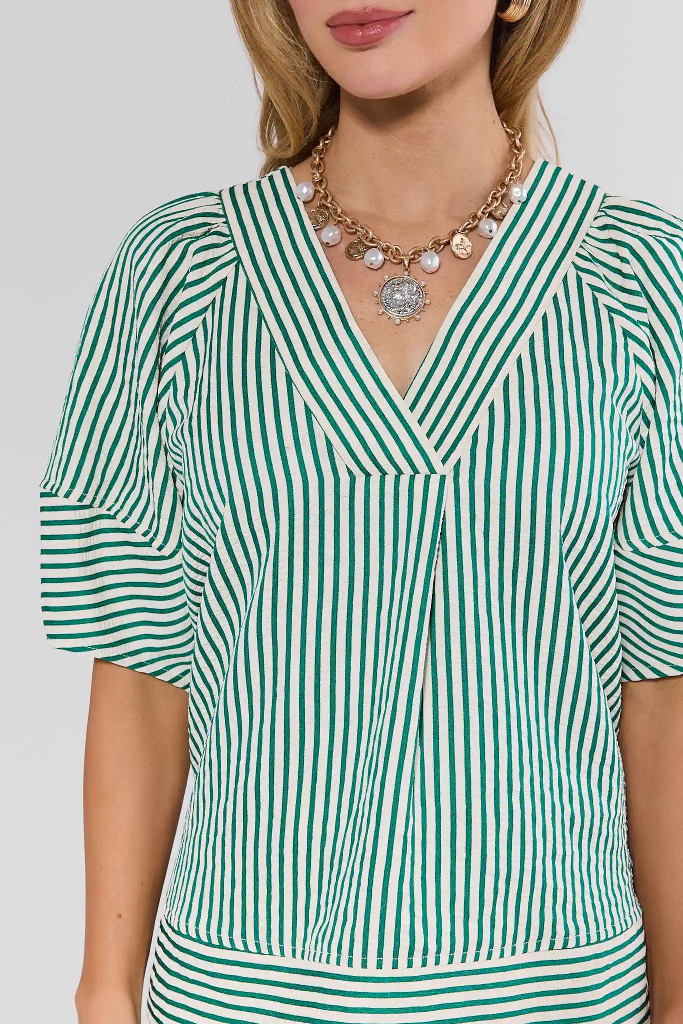Woman wearing a green and white striped dress with a necklace on a plain background