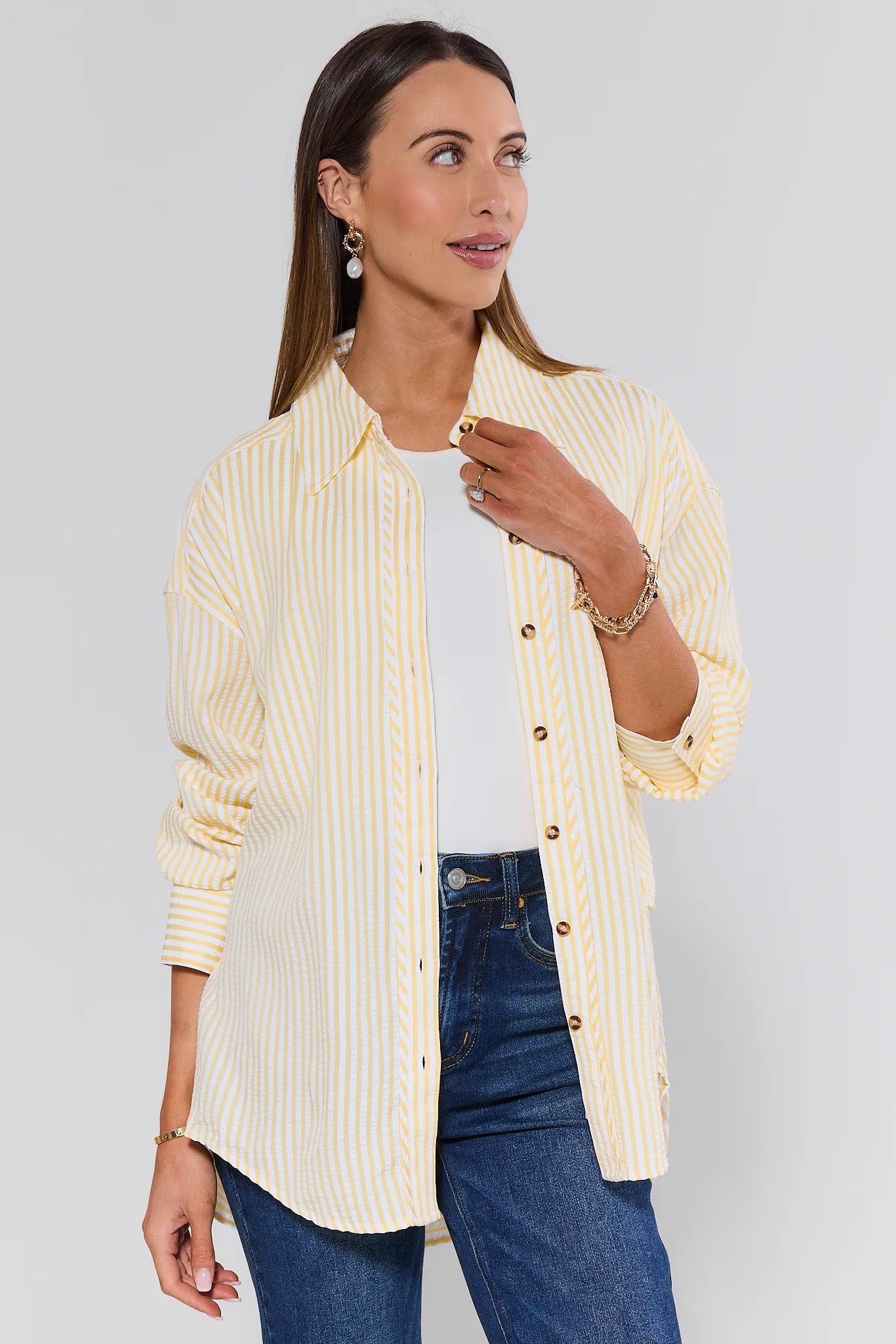 Woman wearing a yellow striped shirt over a white top and blue jeans on a plain background