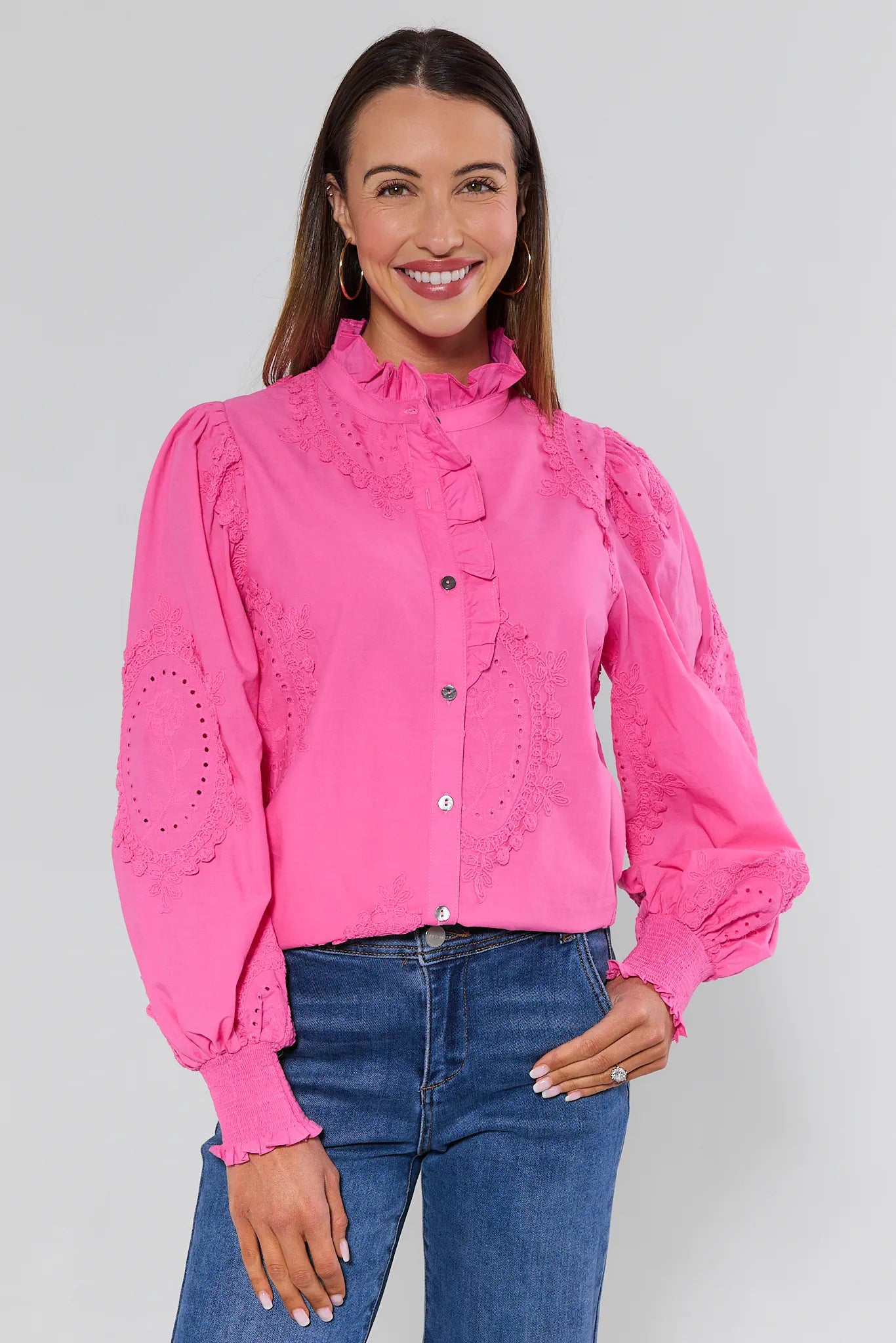 Woman wearing a bright pink blouse with lace details and blue jeans on a white background