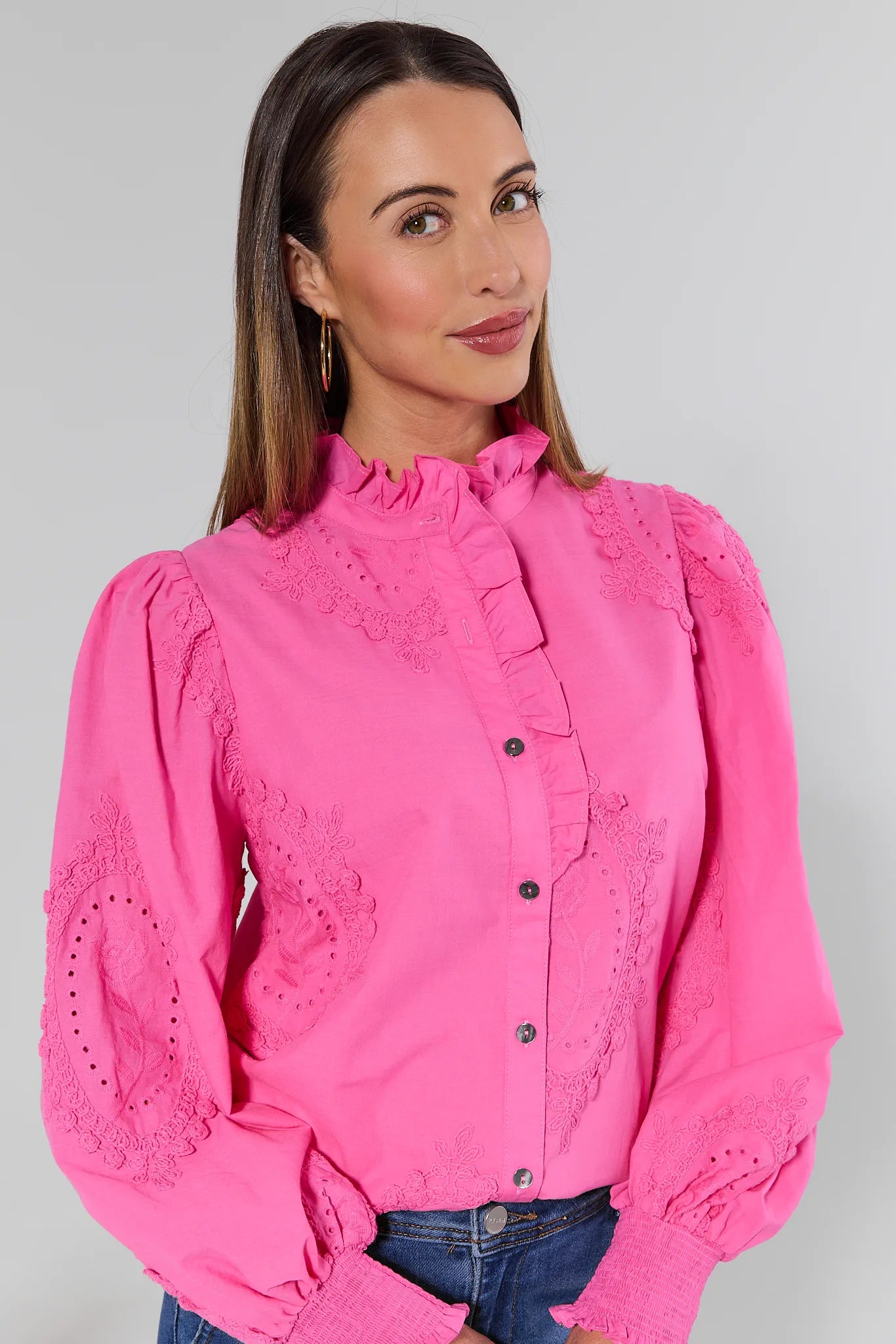 Woman wearing a bright pink blouse with ruffled details on a gray background