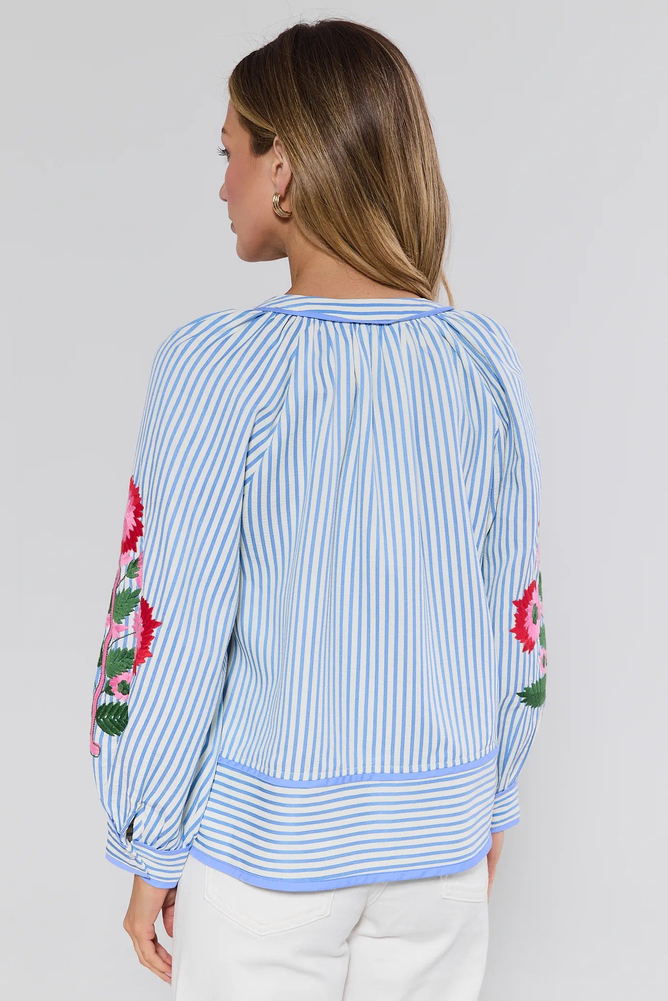 Woman wearing a blue and white striped blouse with floral embroidery on a plain background