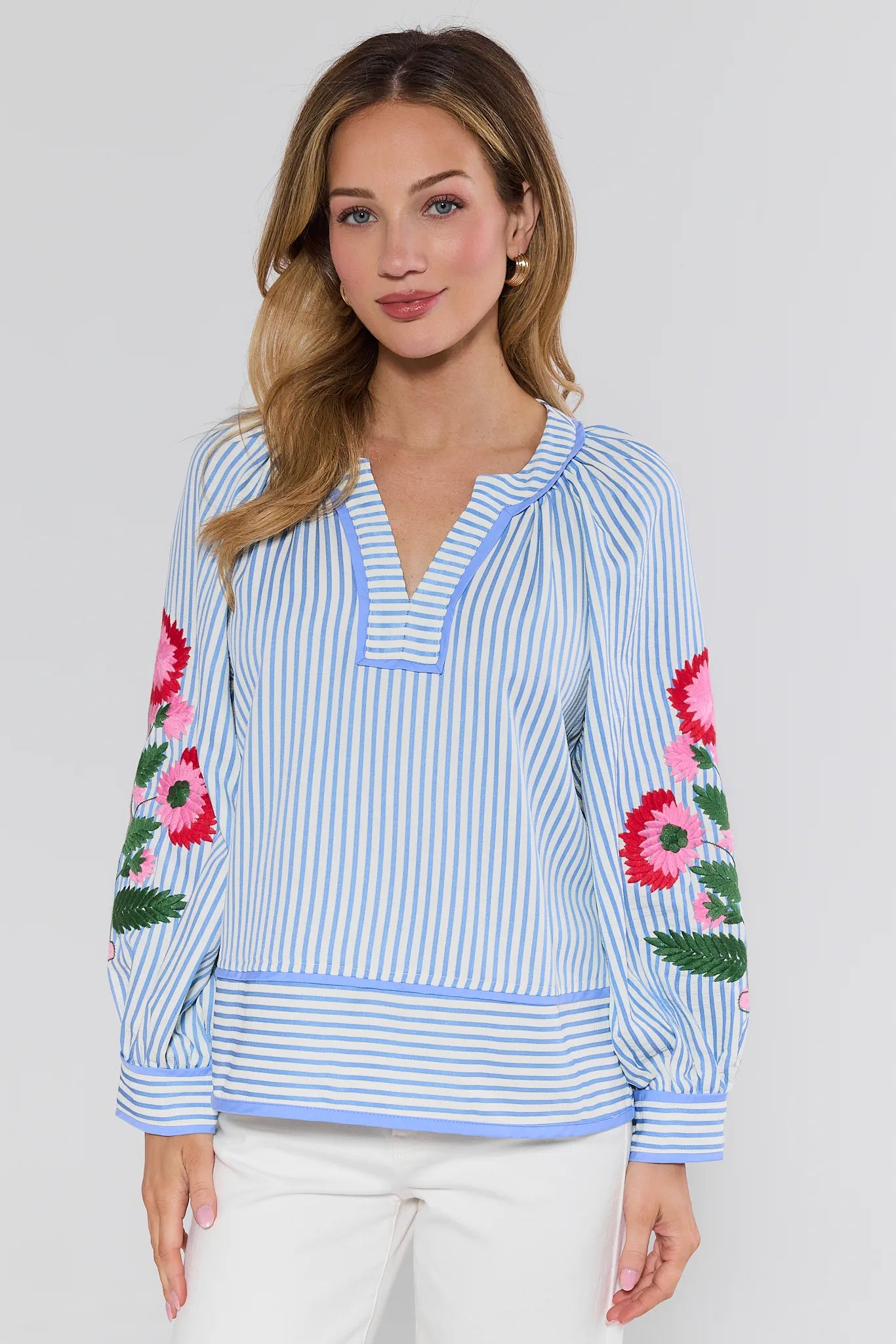 Woman wearing a blue and white striped blouse with floral embroidery on a plain background
