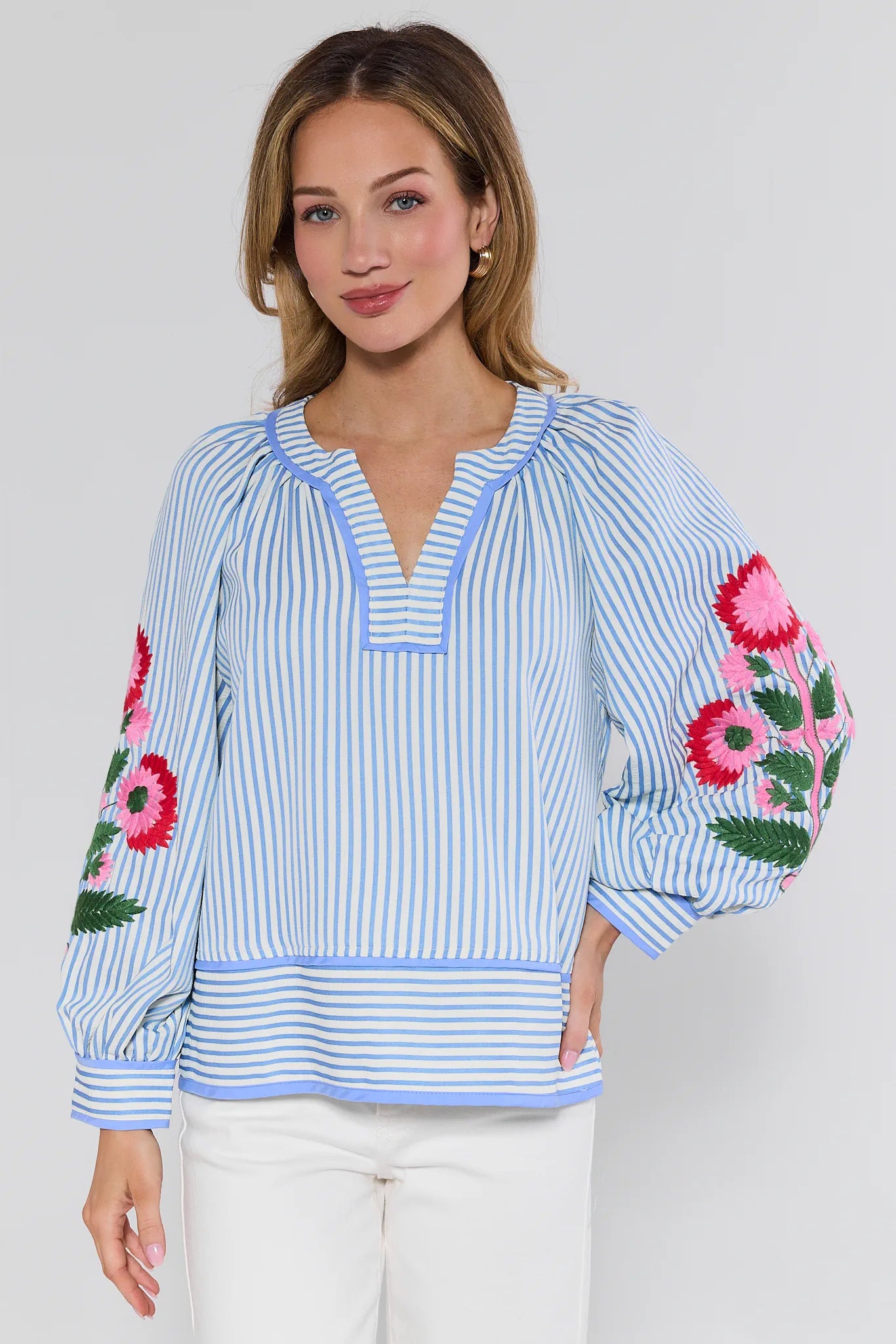 Woman wearing a blue and white striped blouse with floral embroidery on a plain background