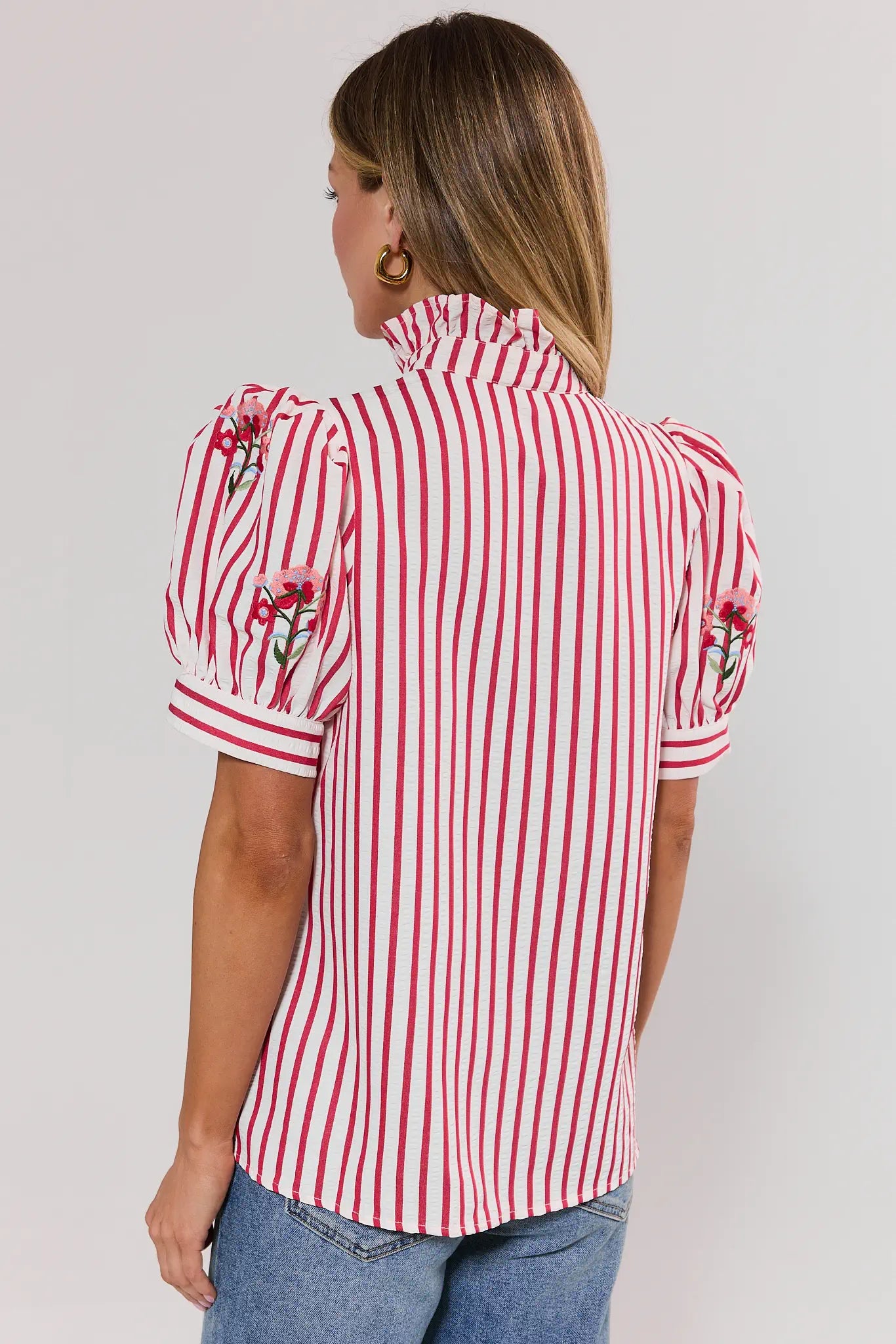 Woman wearing a red and white striped shirt with floral accents on a plain background