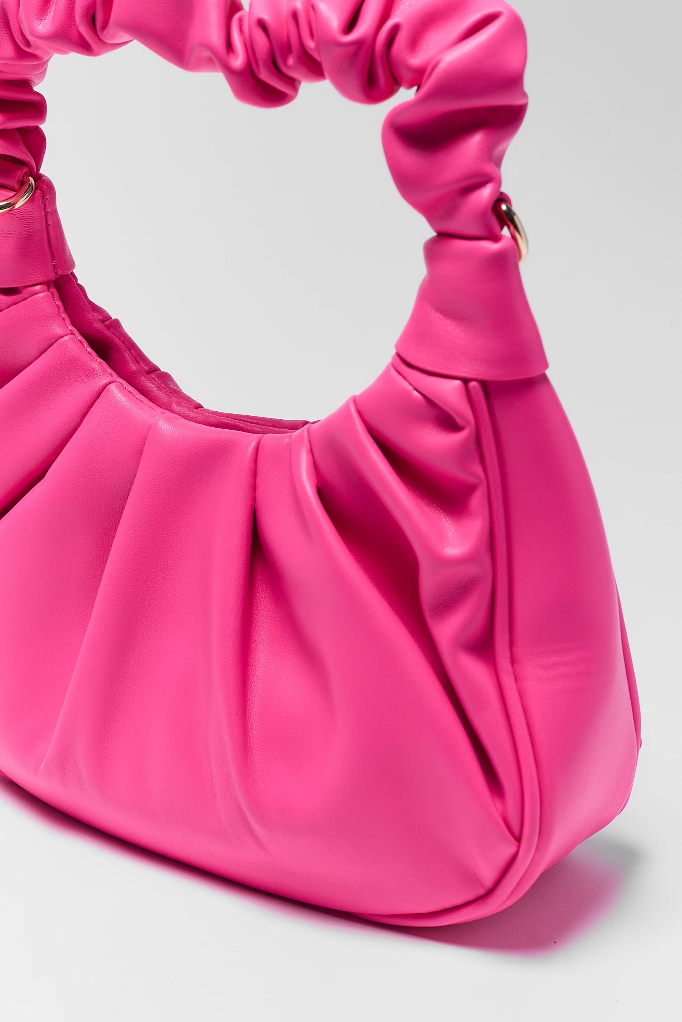 Pink handbag with a ruched handle on a light gray background