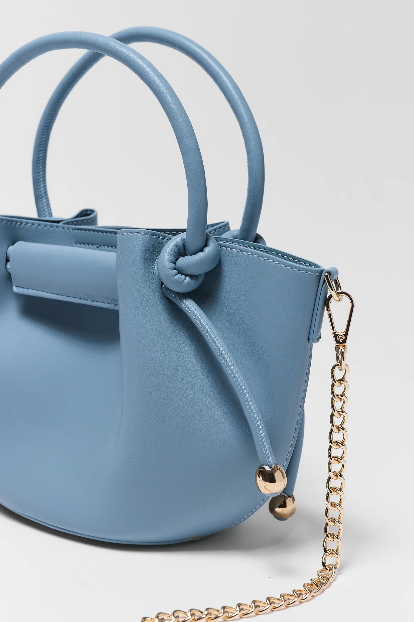 close up Blue handbag with a gold chain on a light gray background