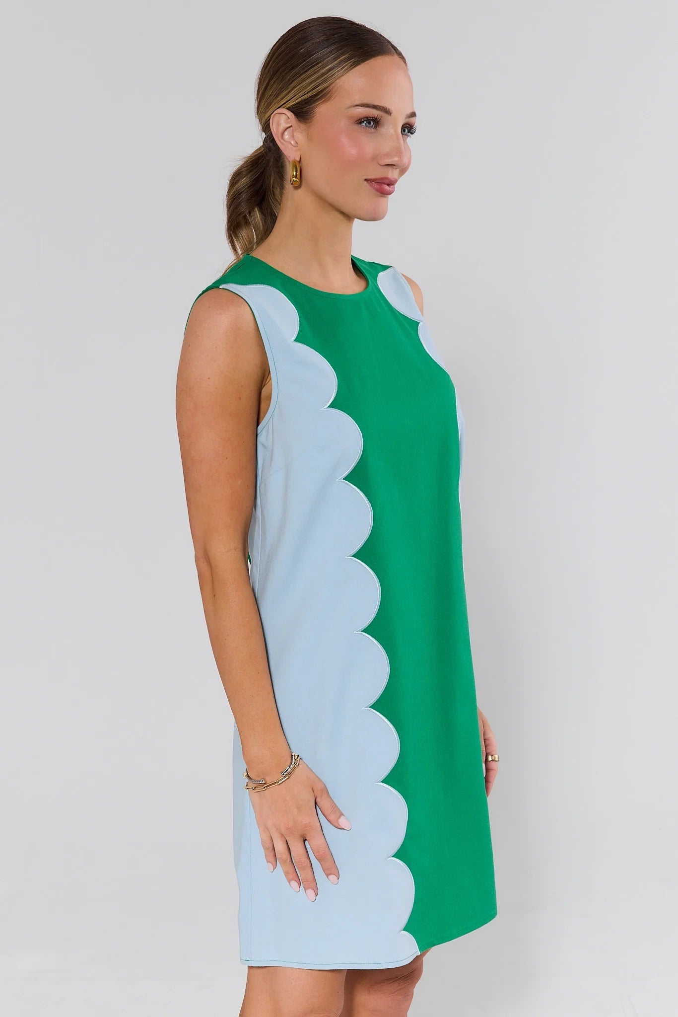 side shot Woman wearing a green and light blue dress with scalloped edges on a plain background