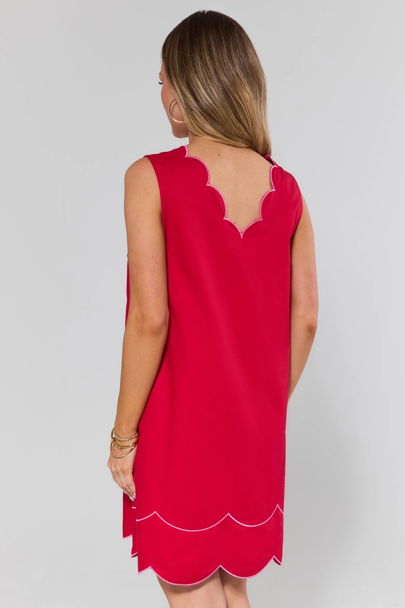 Woman standing wearing a red sleeveless dress with scalloped edges on a plain background