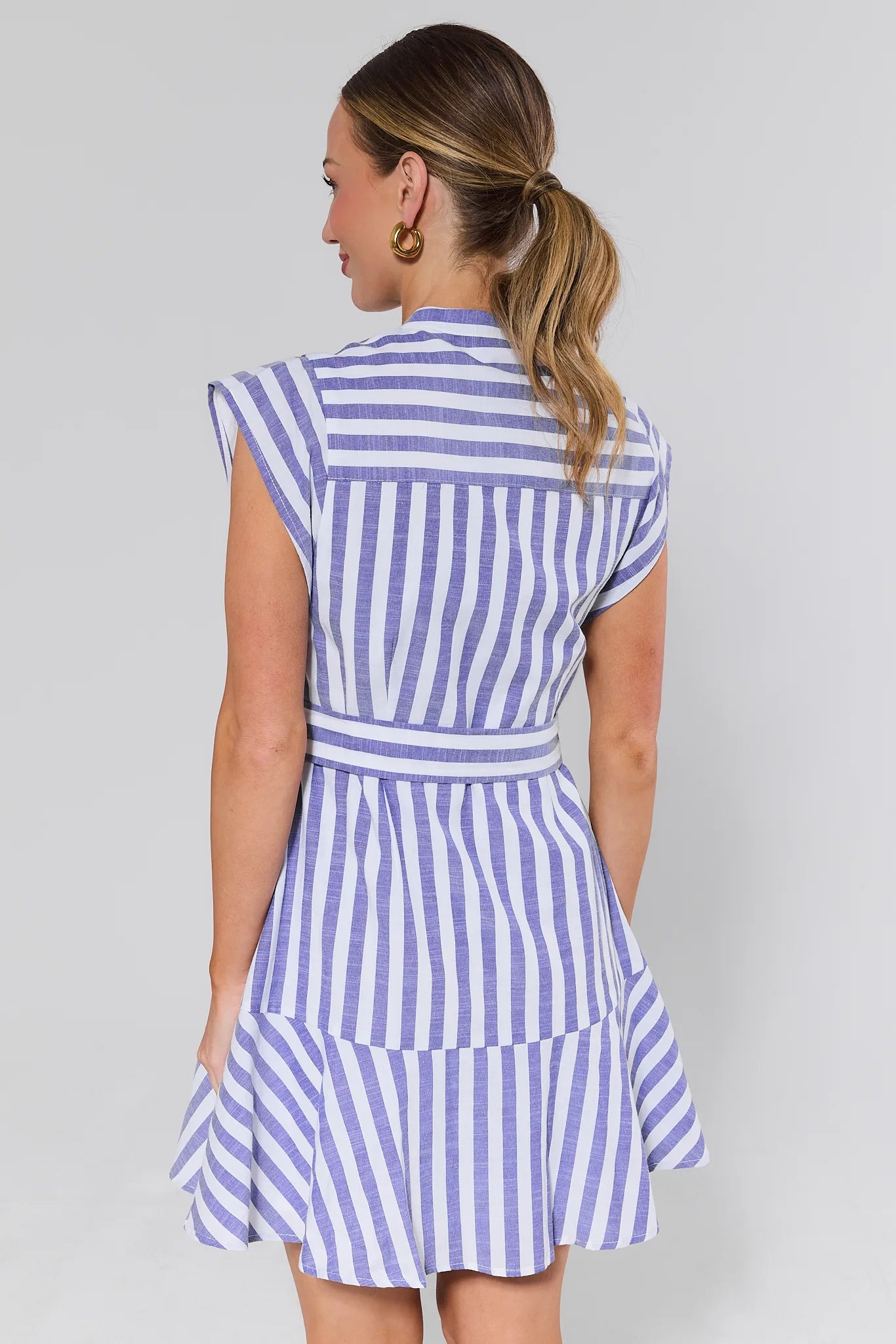 Woman standing wearing a blue and white striped dress against a plain background