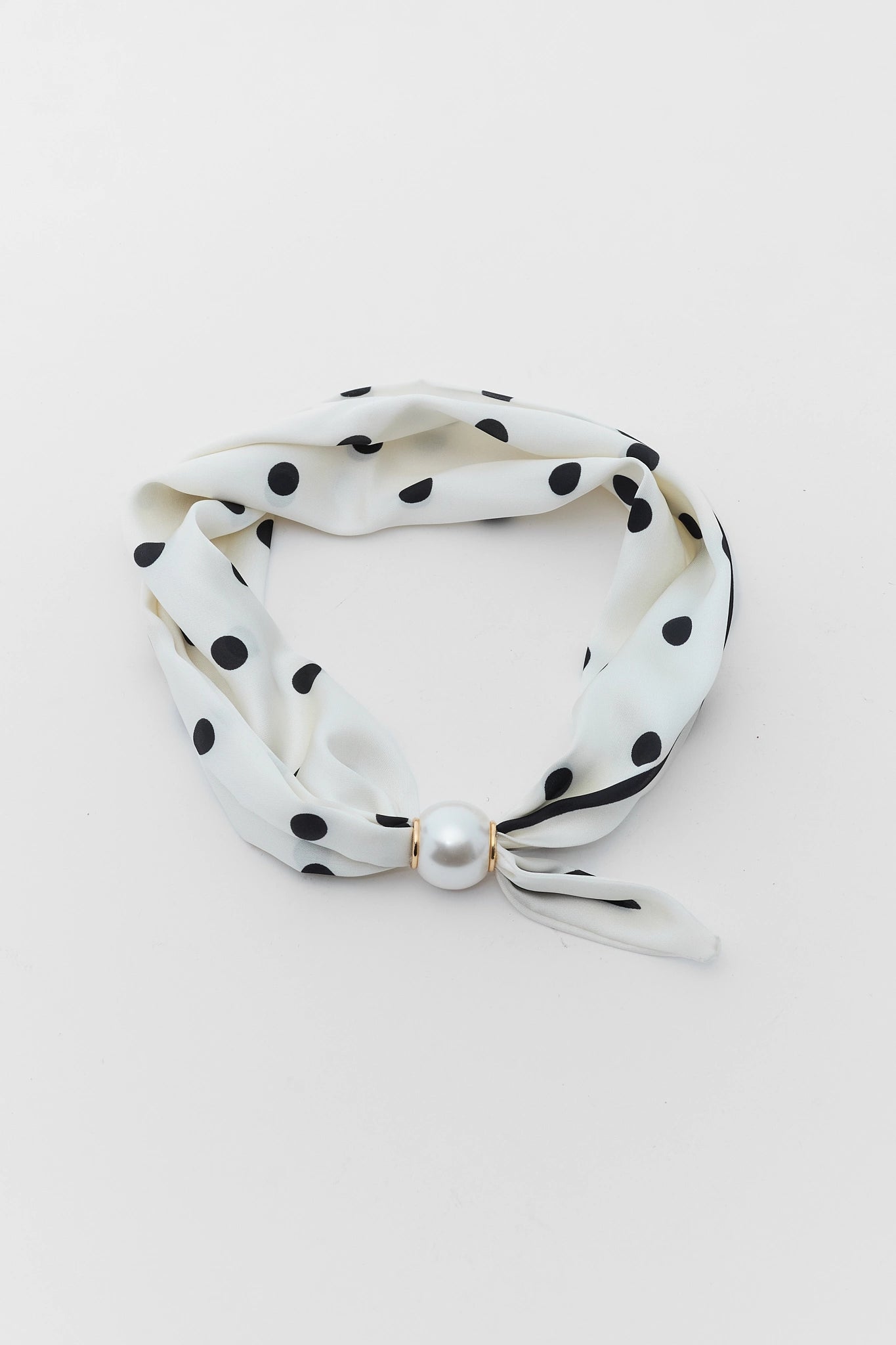 White headband with black polka dots and a pearl accent on a light gray background