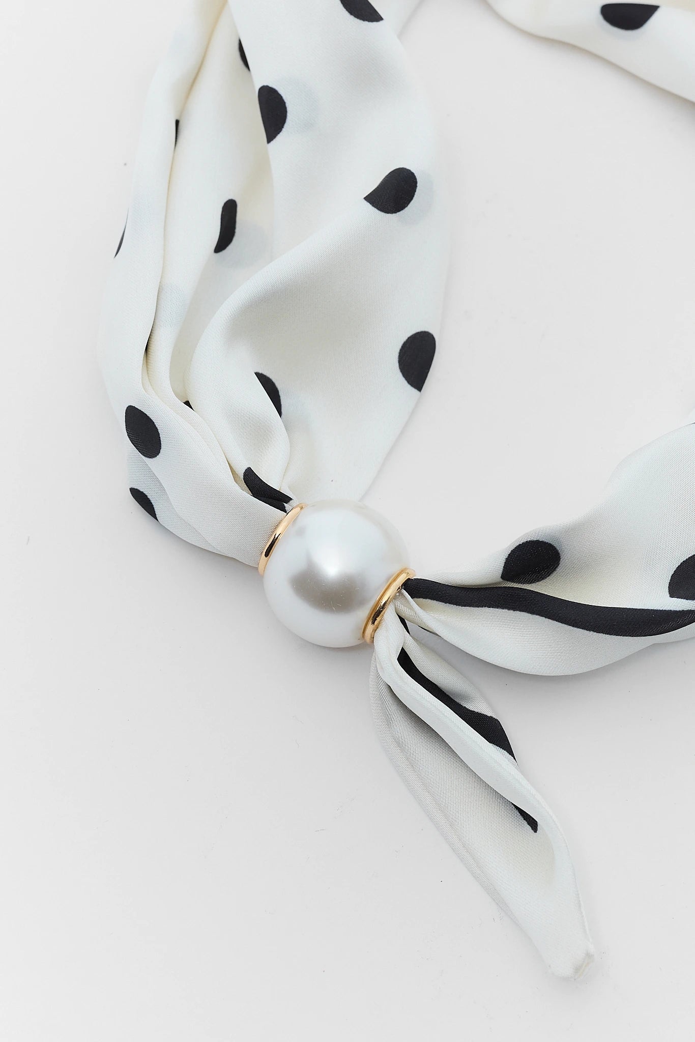 White scarf with black polka dots and a pearl-like knot on a light gray background