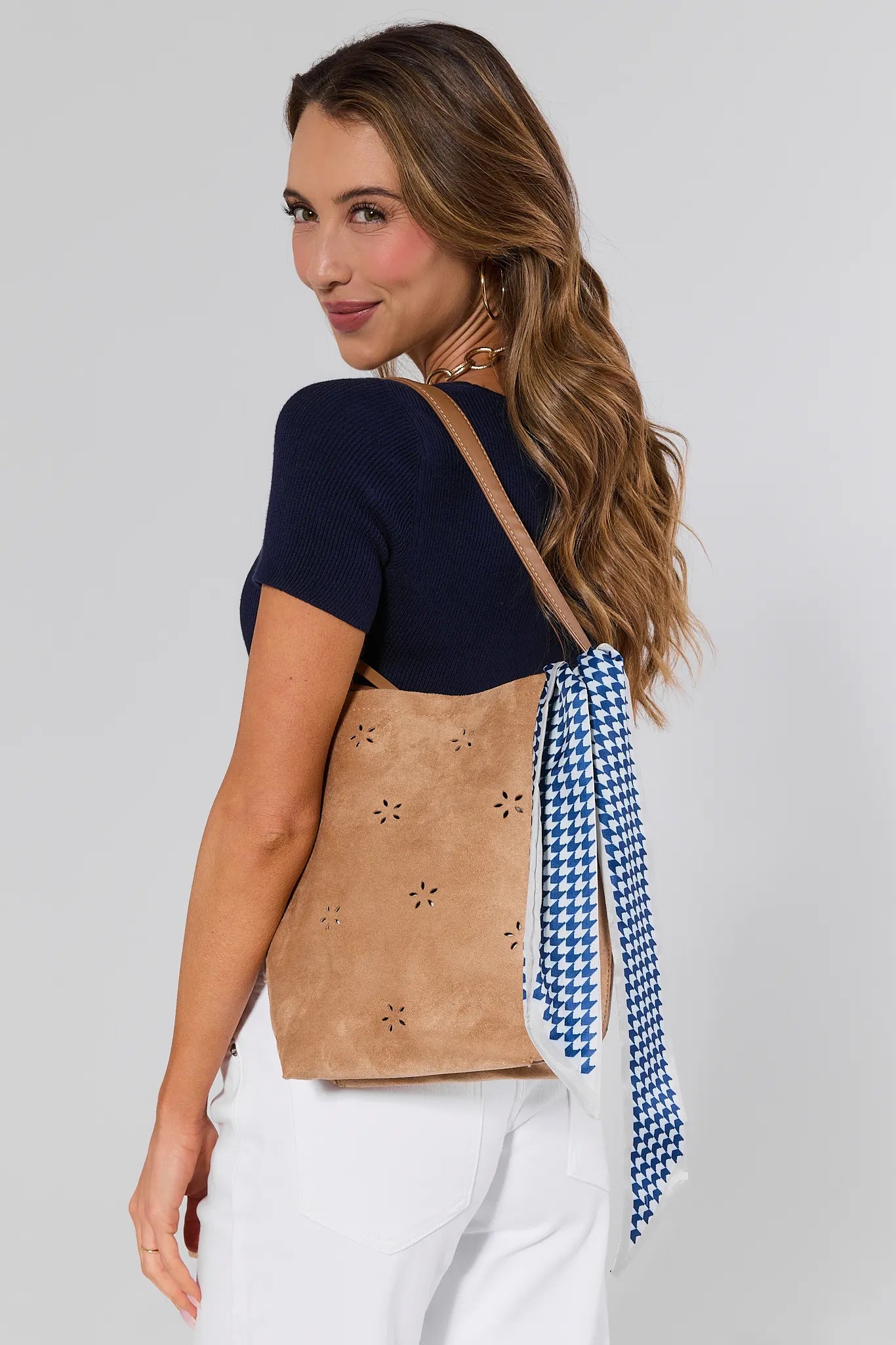 Woman wearing a brown top with cut-out design and a blue and white checkered scarf, on a plain background