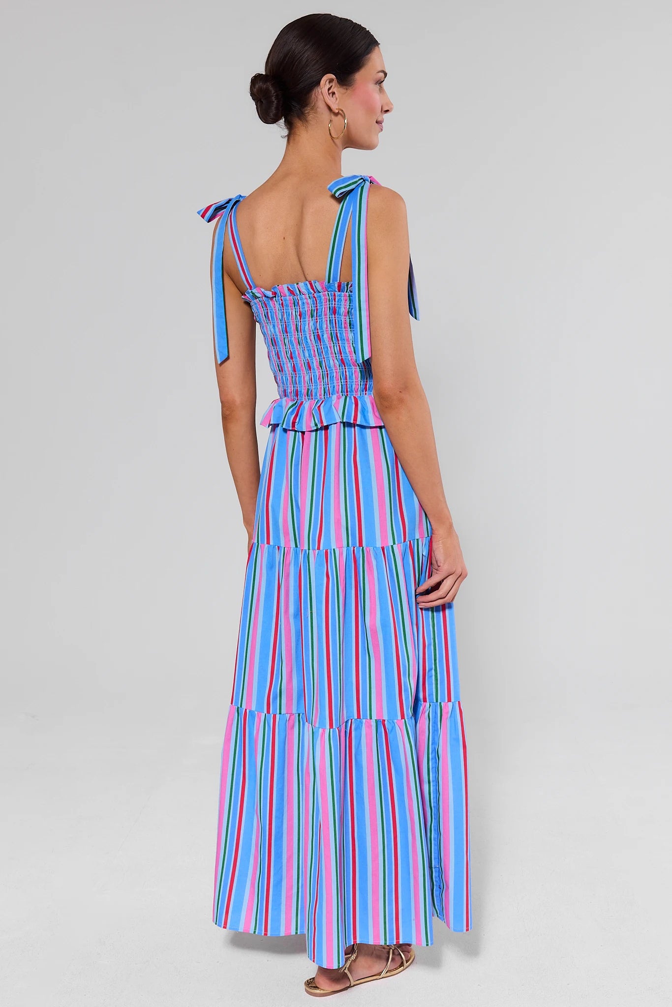 Woman standing wearing a colorful striped dress on a plain background