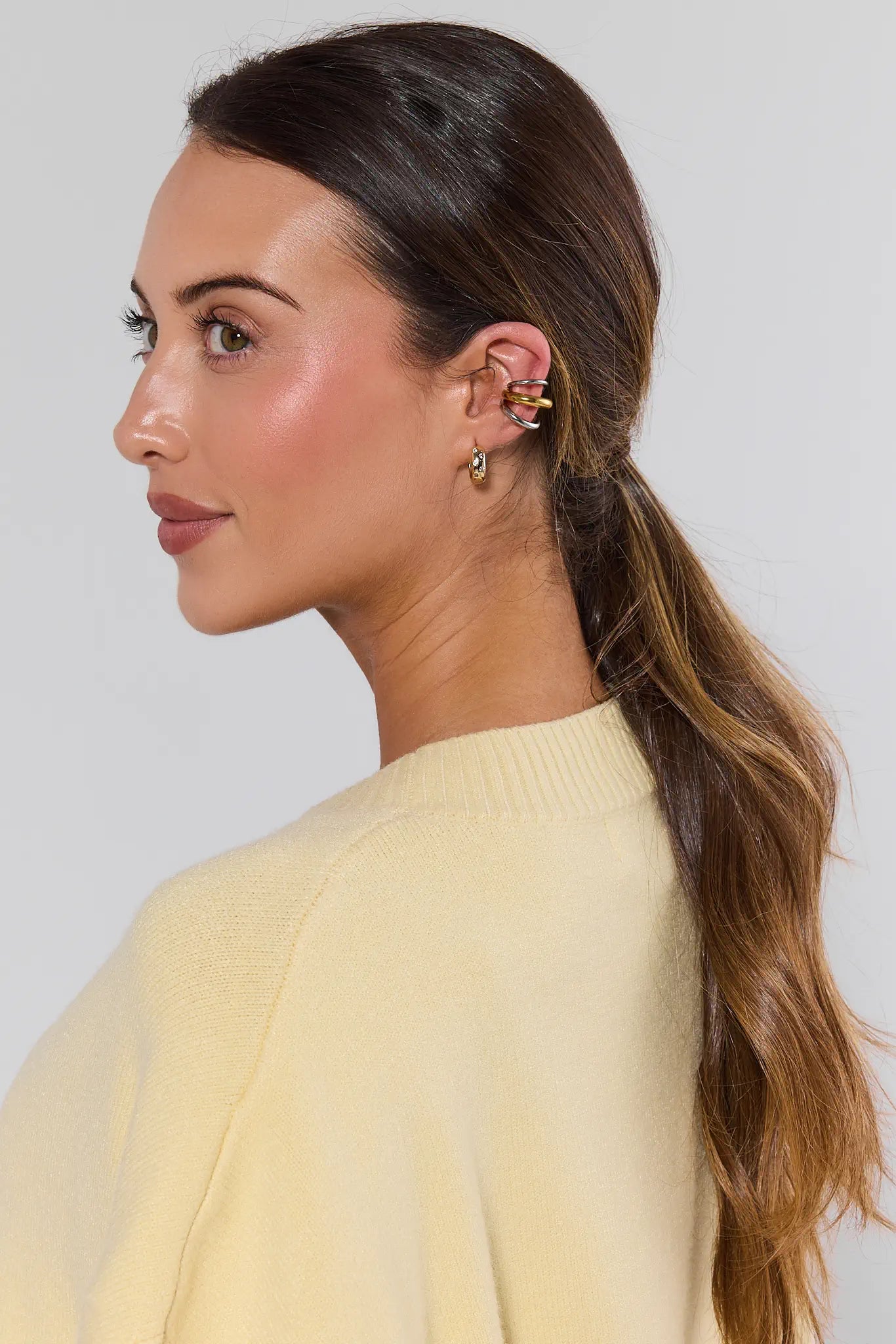 Woman with a ponytail wearing earrings against a plain background