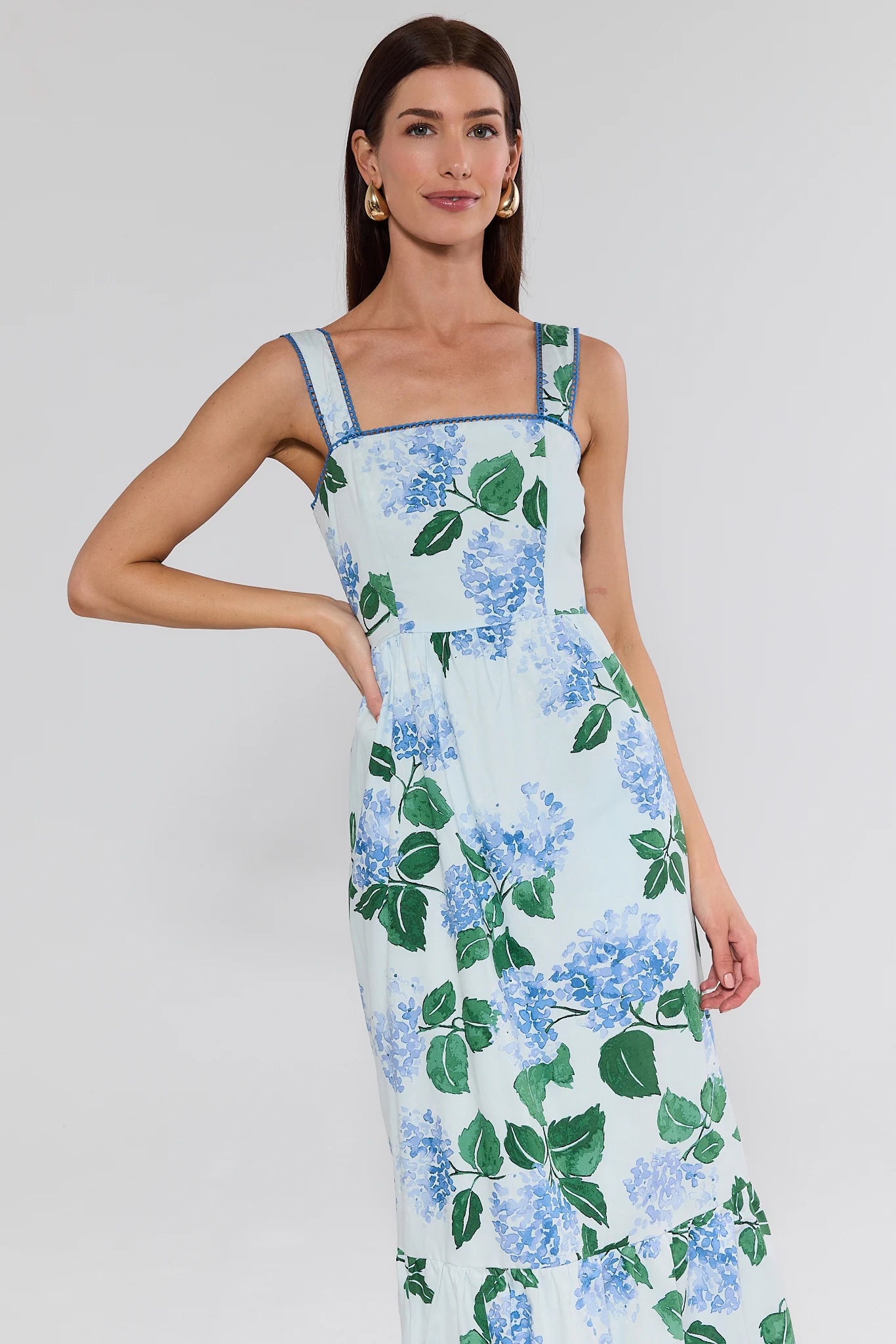 Woman wearing a floral dress with blue flowers and green leaves on a plain background