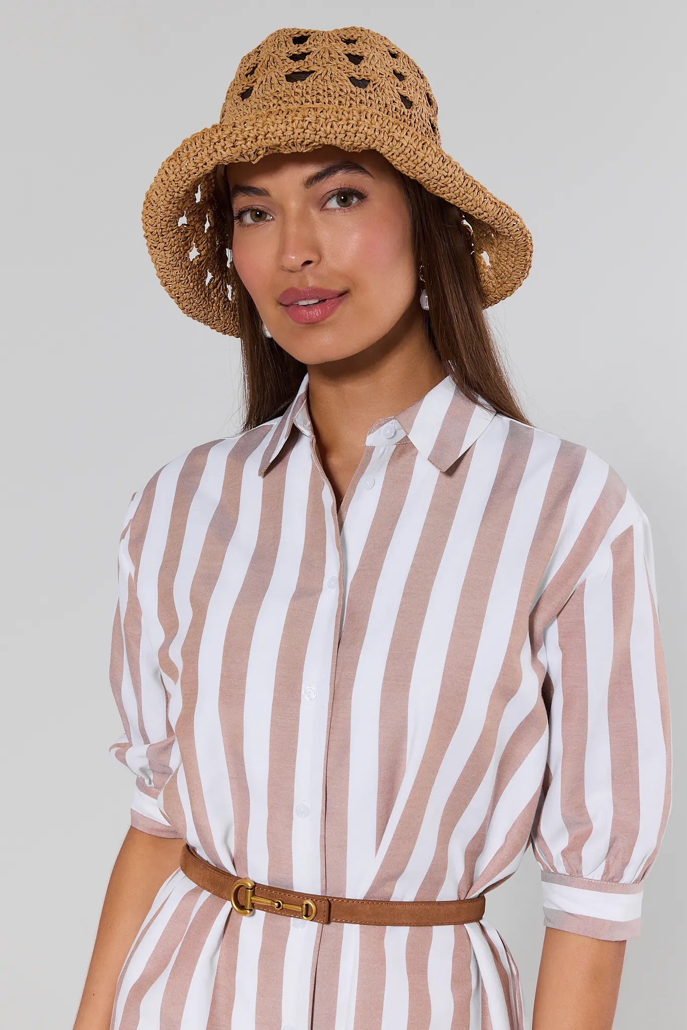 Woman wearing a striped shirt and straw hat against a plain background