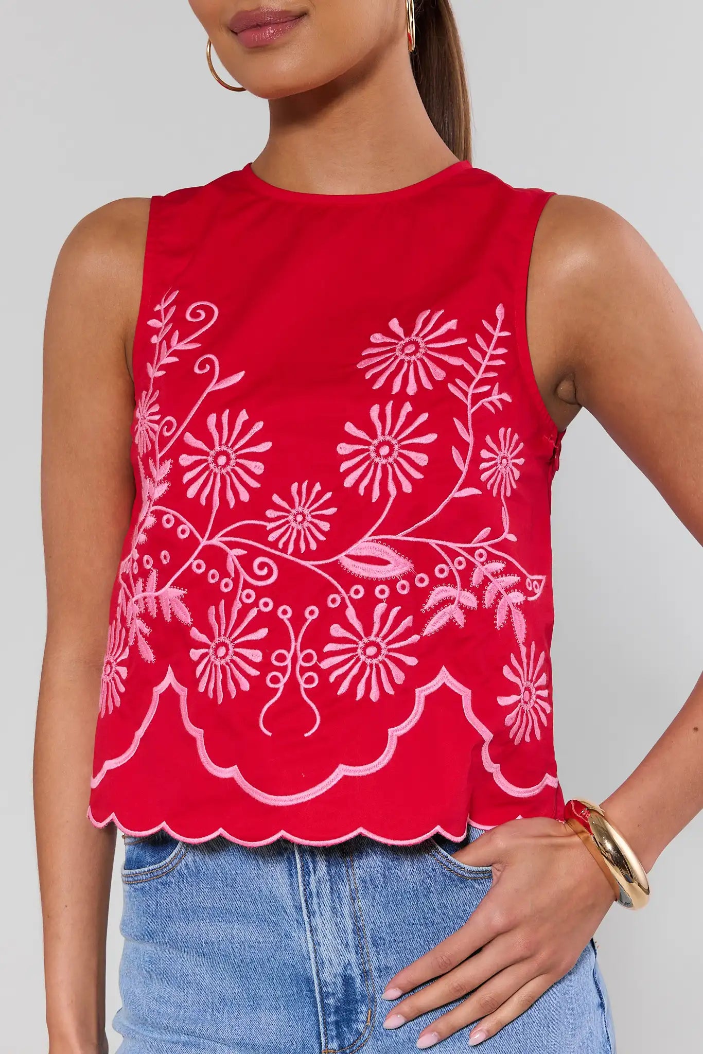 close up Red sleeveless top with white floral patterns worn by a person on a plain background