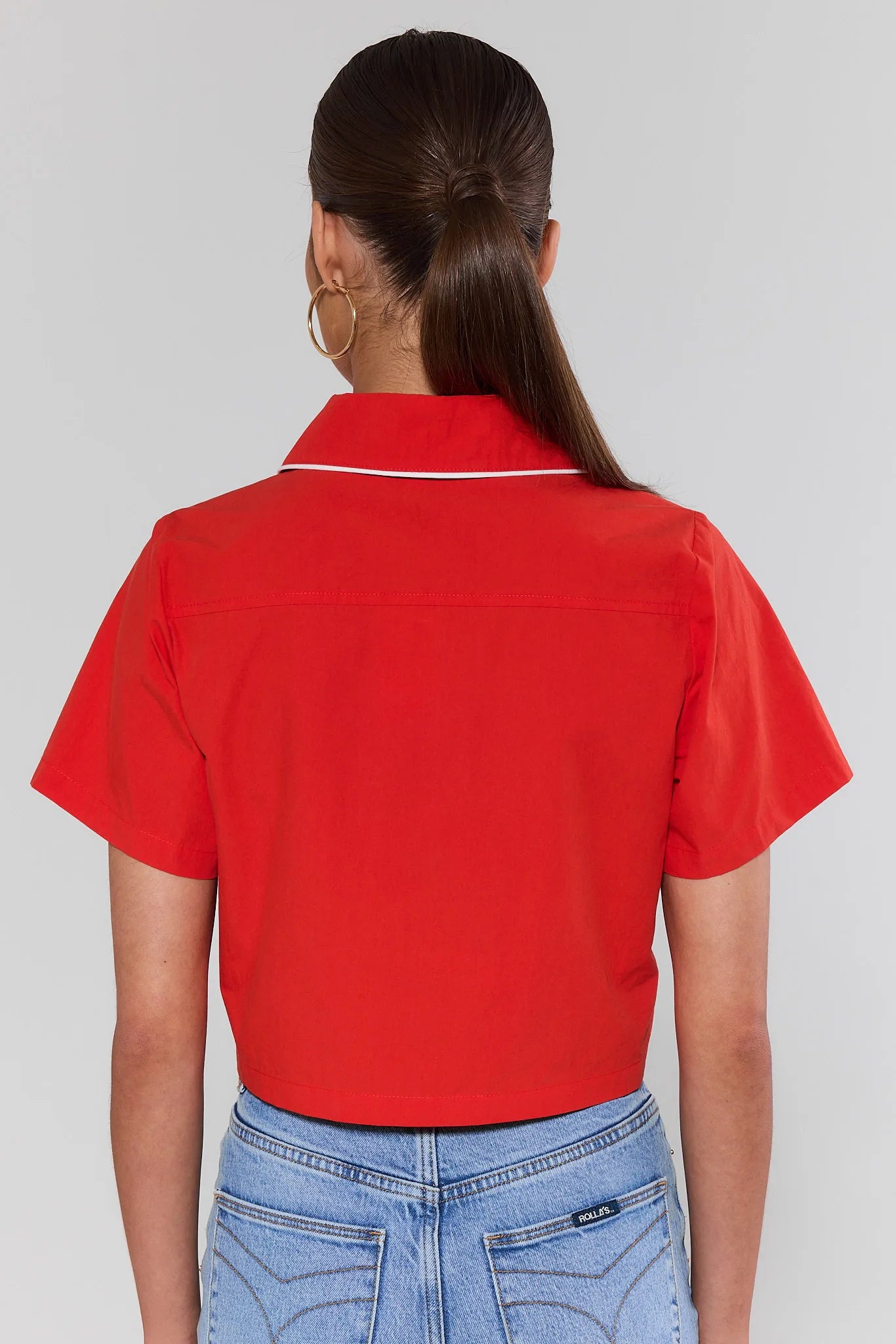 Person standing wearing a red polo shirt and blue jeans on a plain background