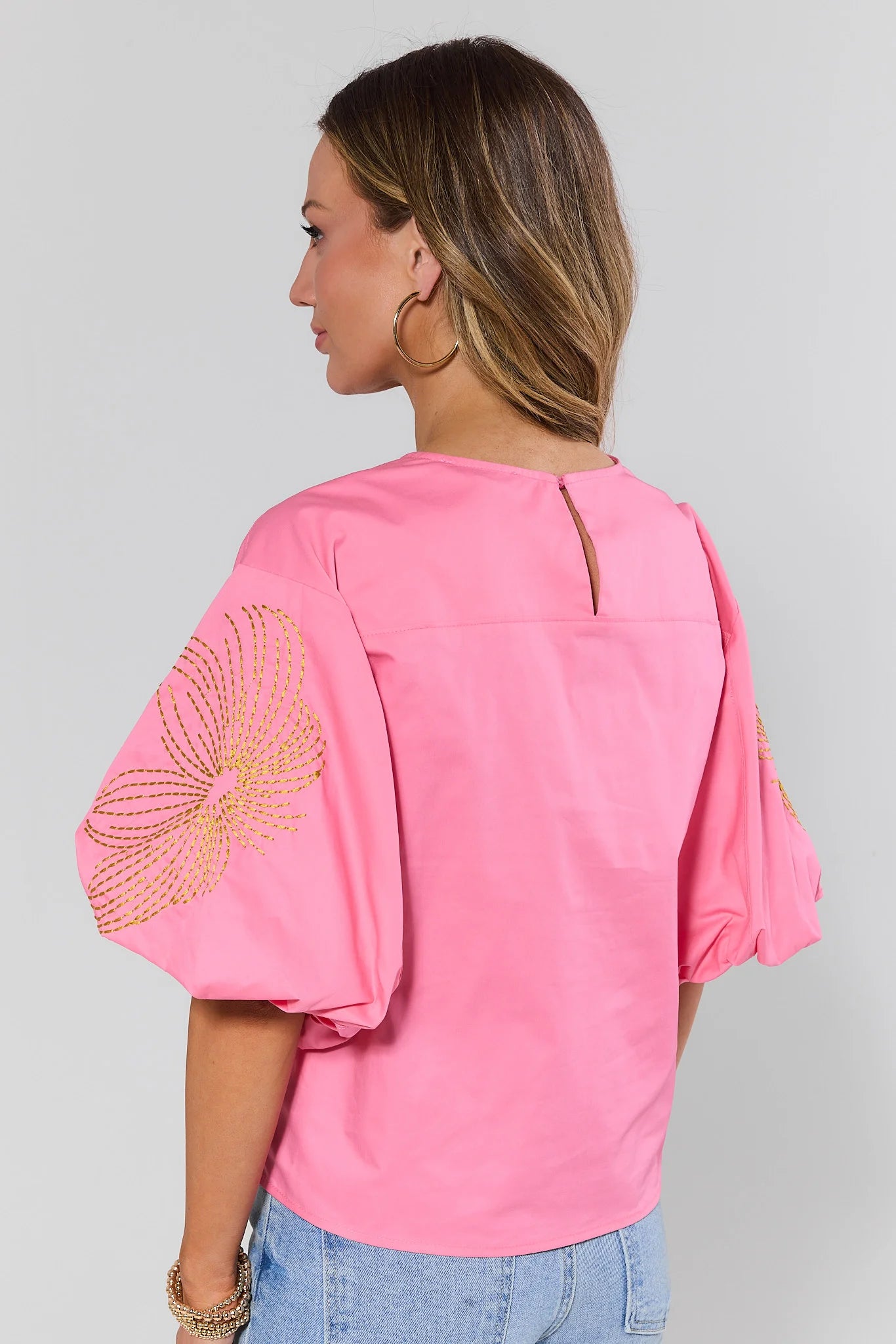 Woman standing wearing a pink blouse with embellished sleeves on a gray background