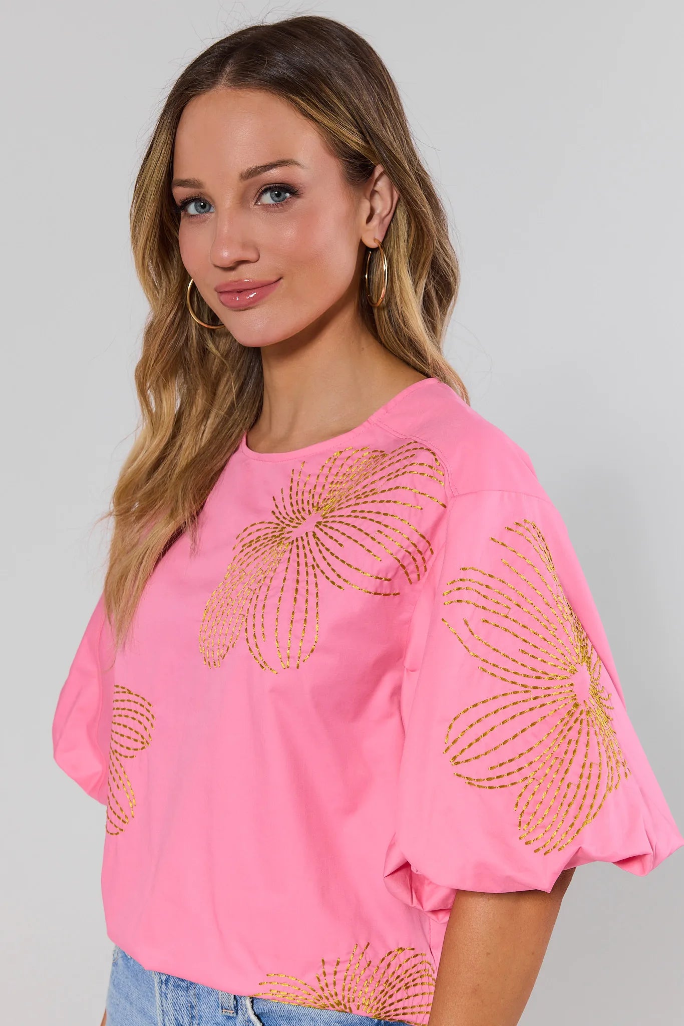 close up Woman wearing a pink blouse with gold floral patterns on a plain background