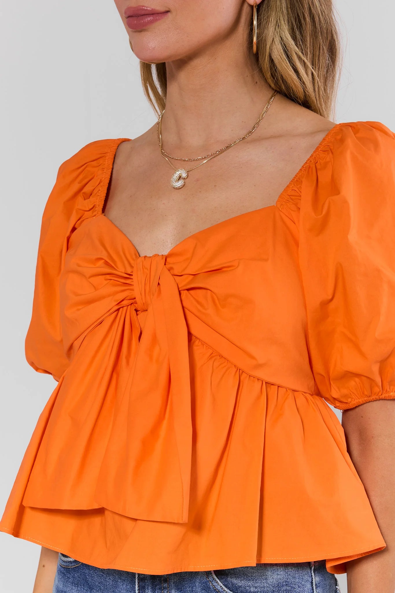 close up Orange blouse with puff sleeves and a tie detail on a plain background