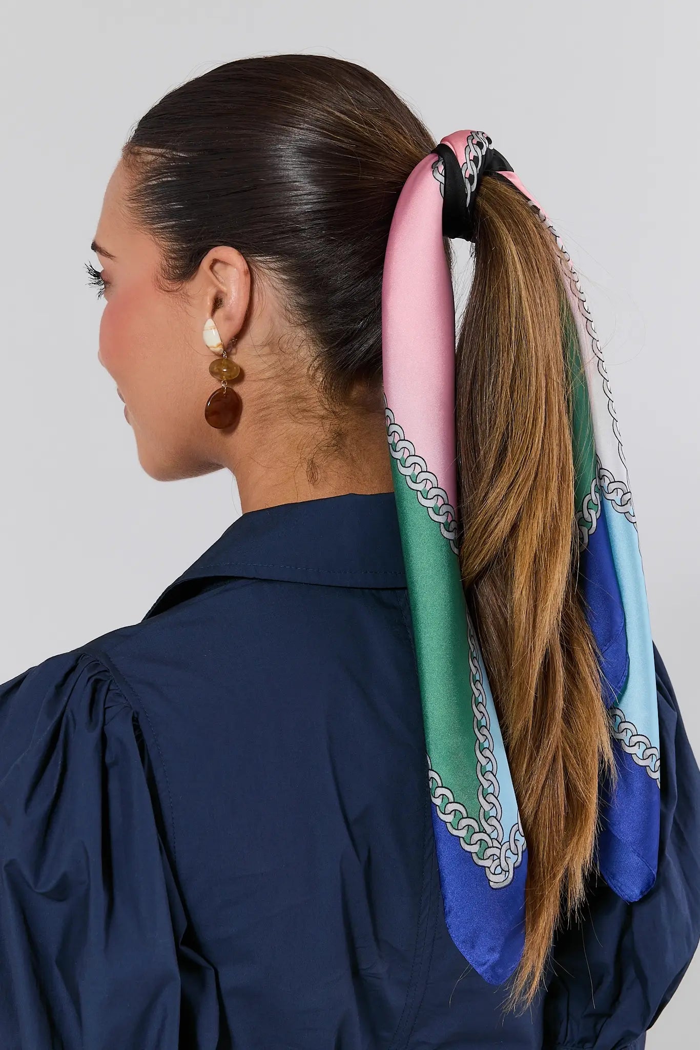 Woman with a colorful scarf tied in a ponytail against a plain background