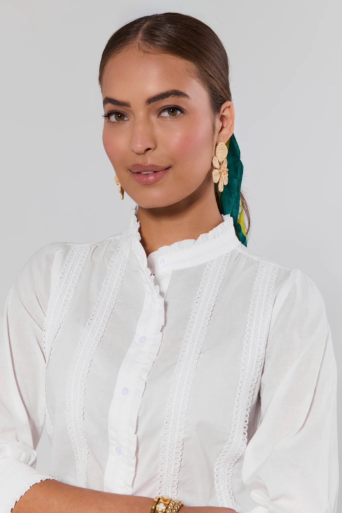 close up Woman wearing a white outfit with green earrings against a light gray background