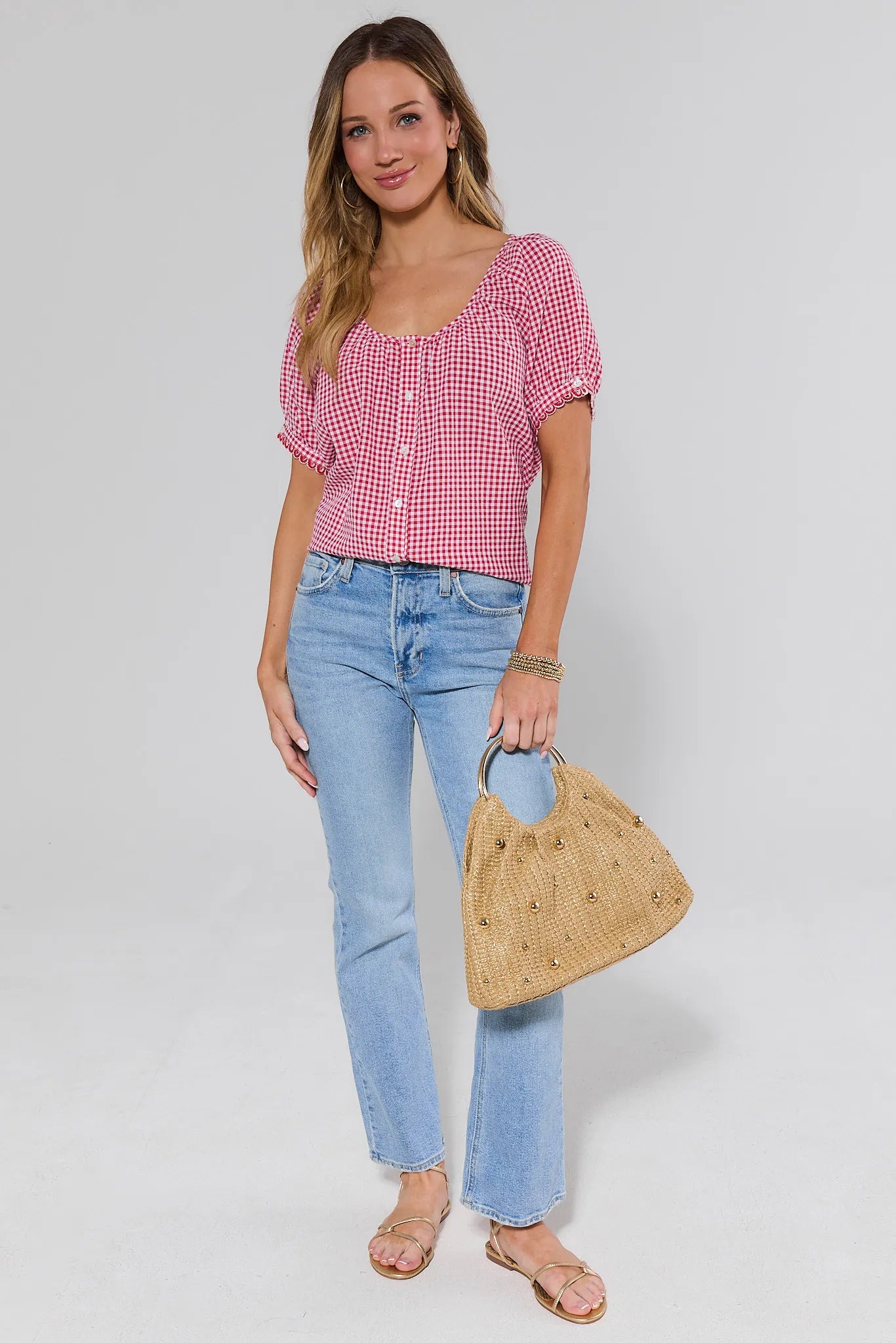 Woman wearing a red and white checkered top and blue jeans, holding a woven bag on a white background