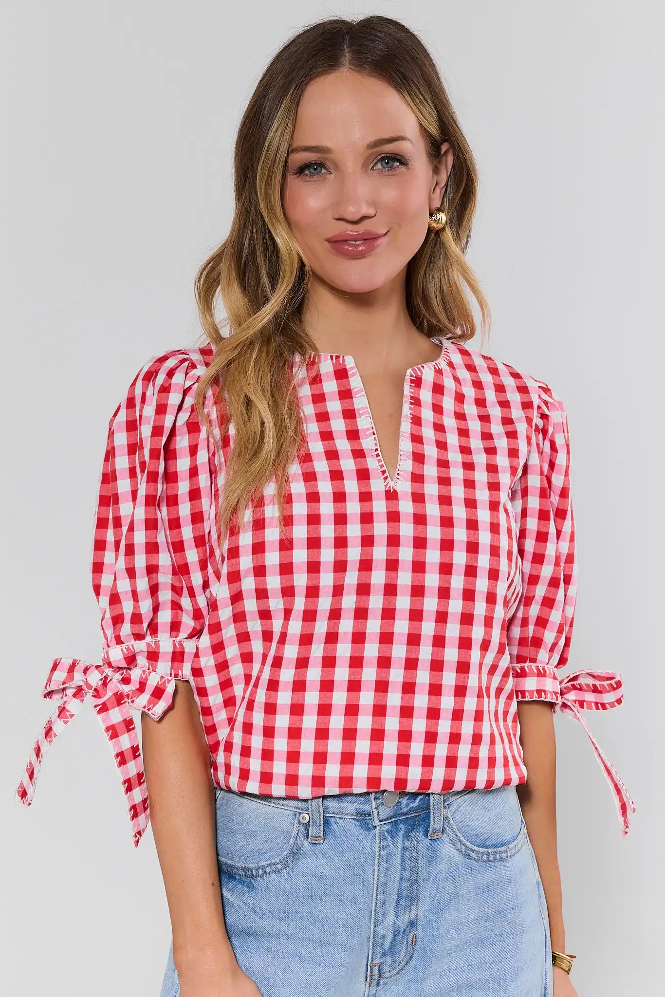 Woman wearing a red and white checkered blouse with tied sleeves against a plain background