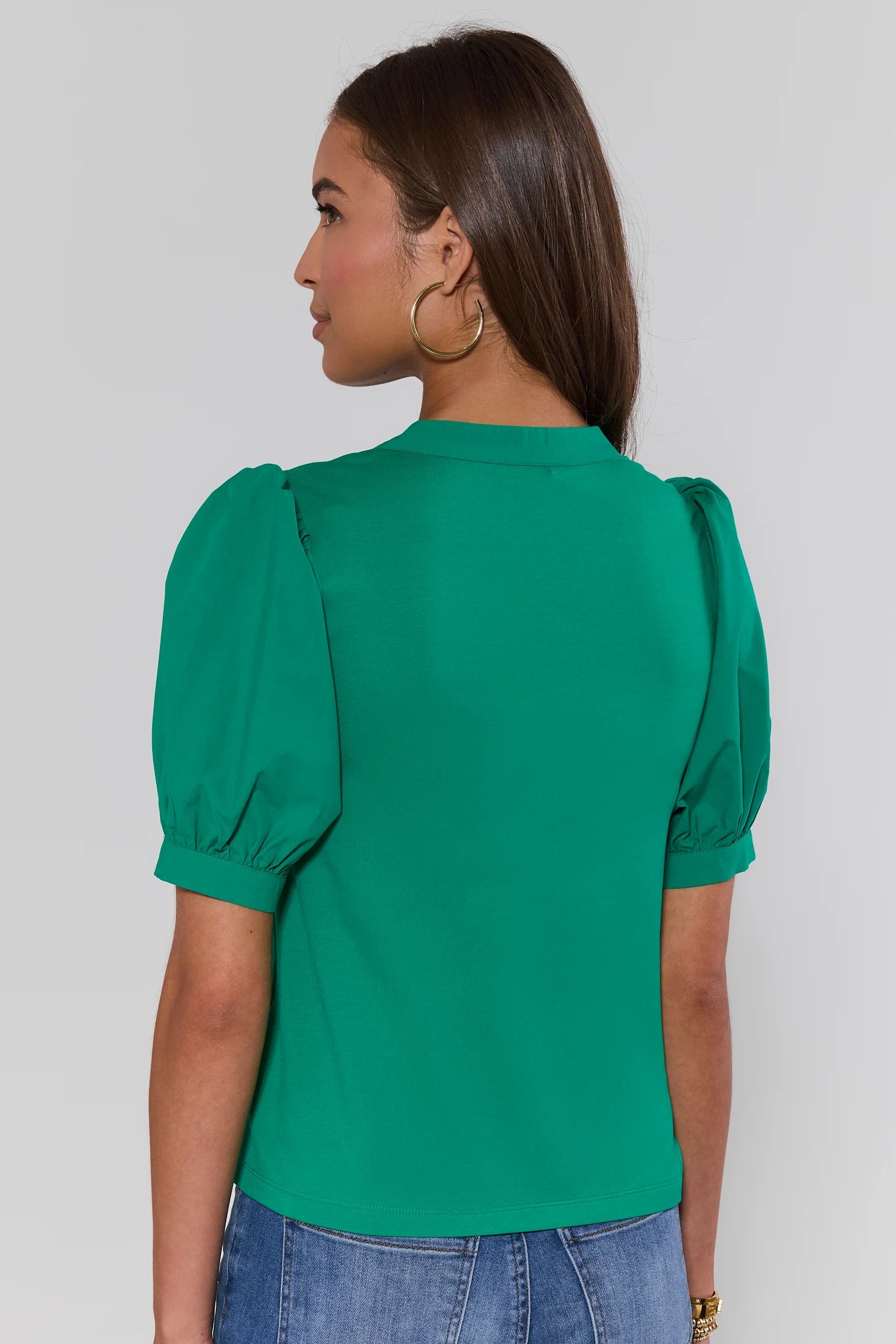 Woman standing wearing a green blouse with puffed sleeves against a plain background