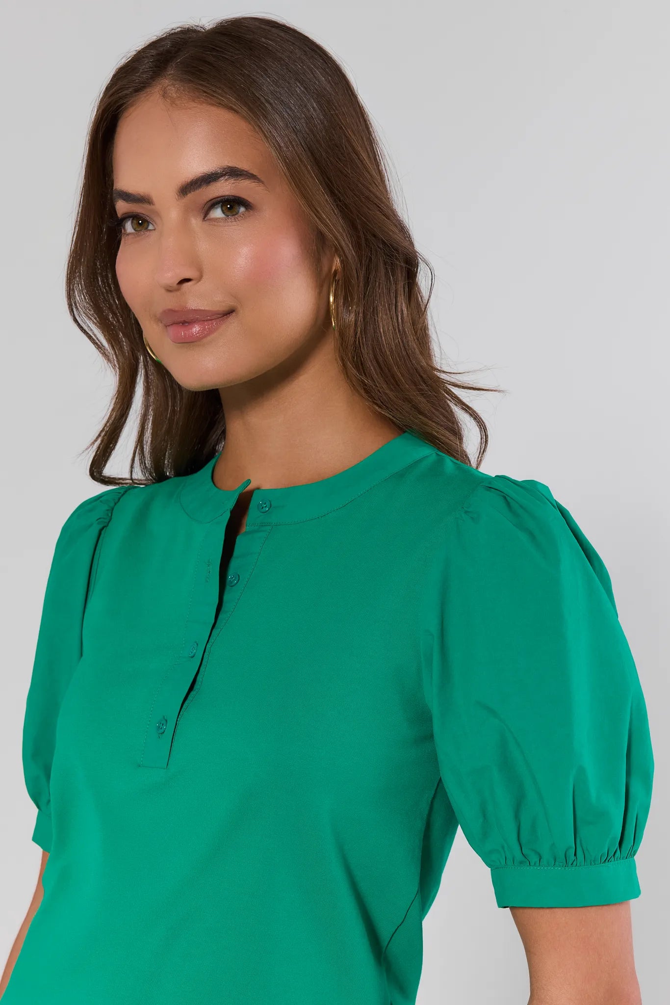 close up Woman wearing a green blouse with puffed sleeves against a plain background