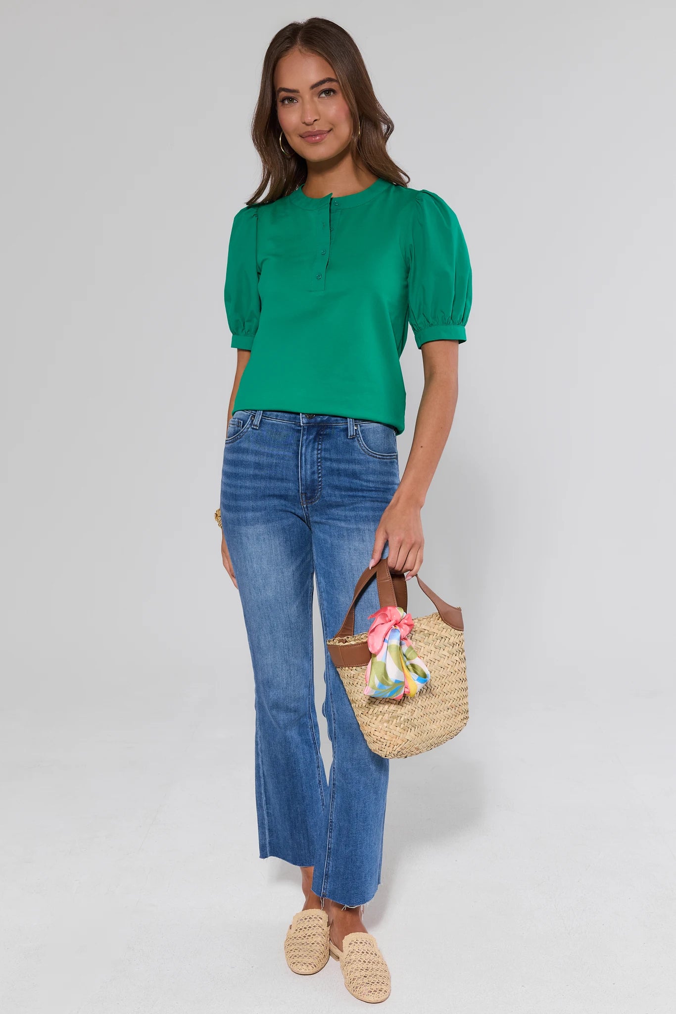 Woman wearing a green top and blue jeans, holding a straw bag with a white background