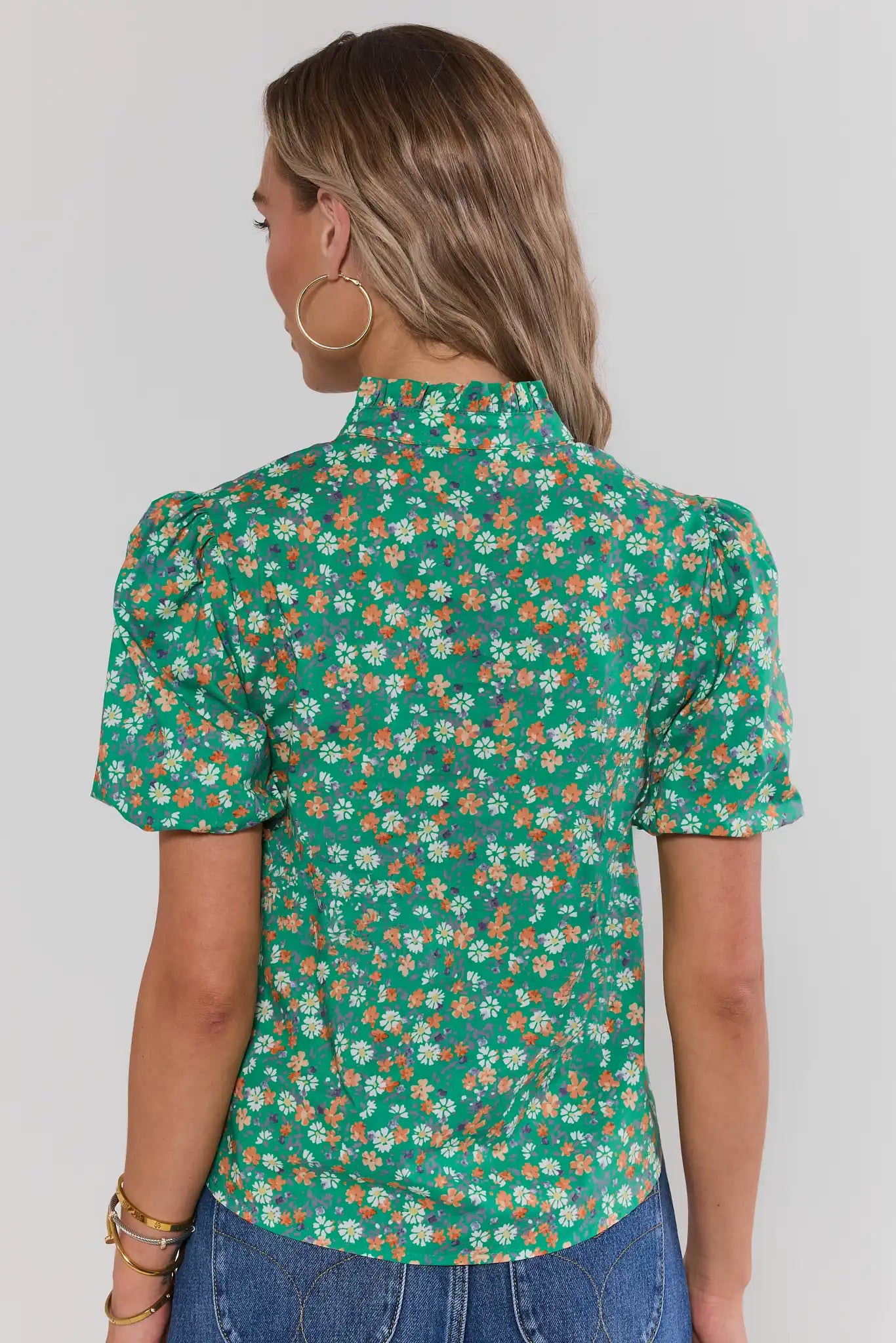 Woman standing wearing a green floral blouse against a white background