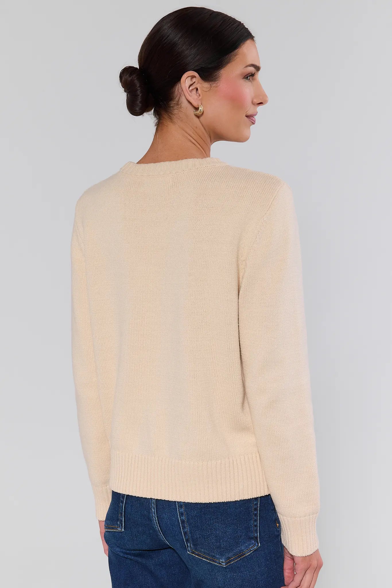 Woman standing wearing a beige sweater and blue jeans on a plain background