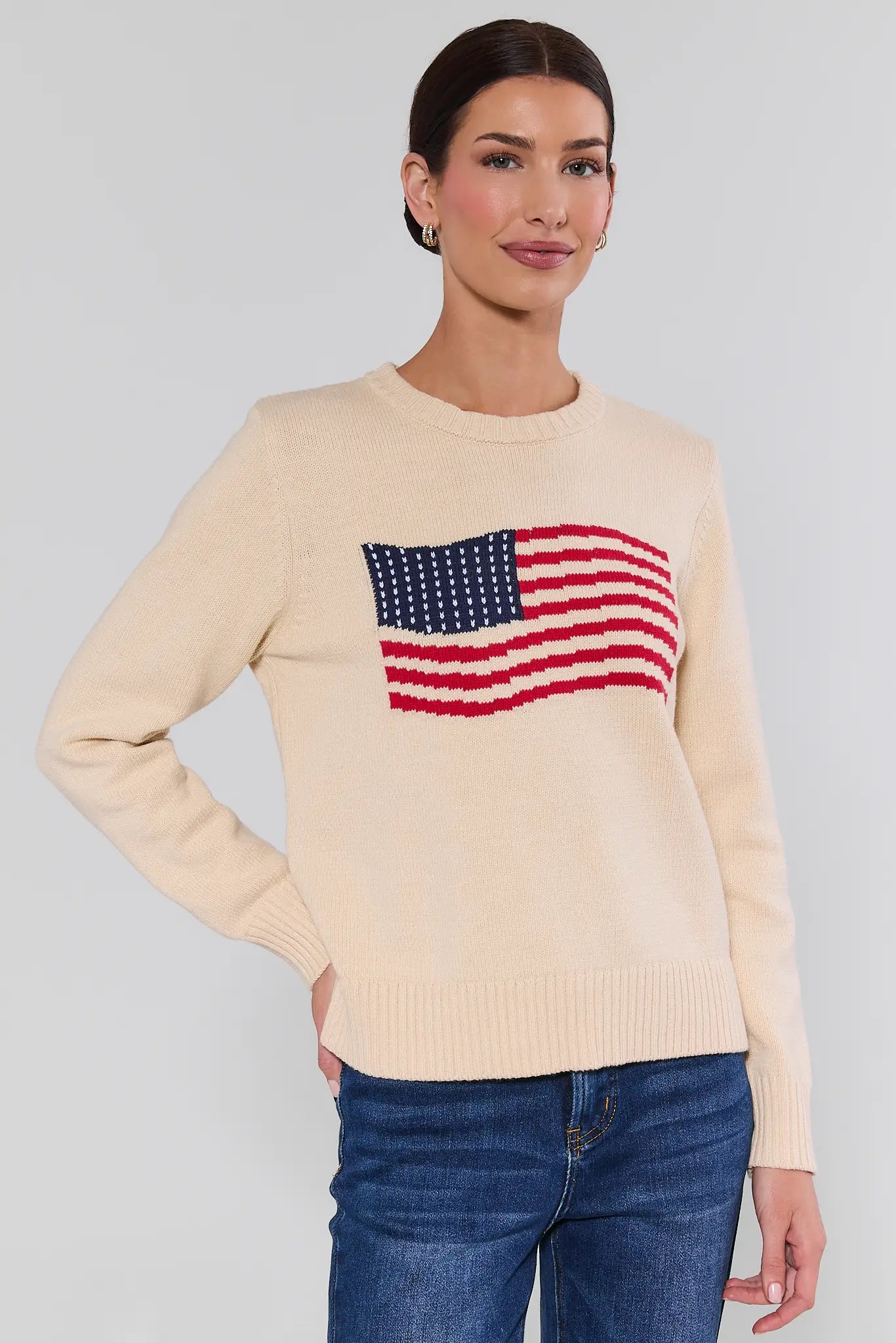 Woman wearing a beige sweater with an American flag design on a plain background