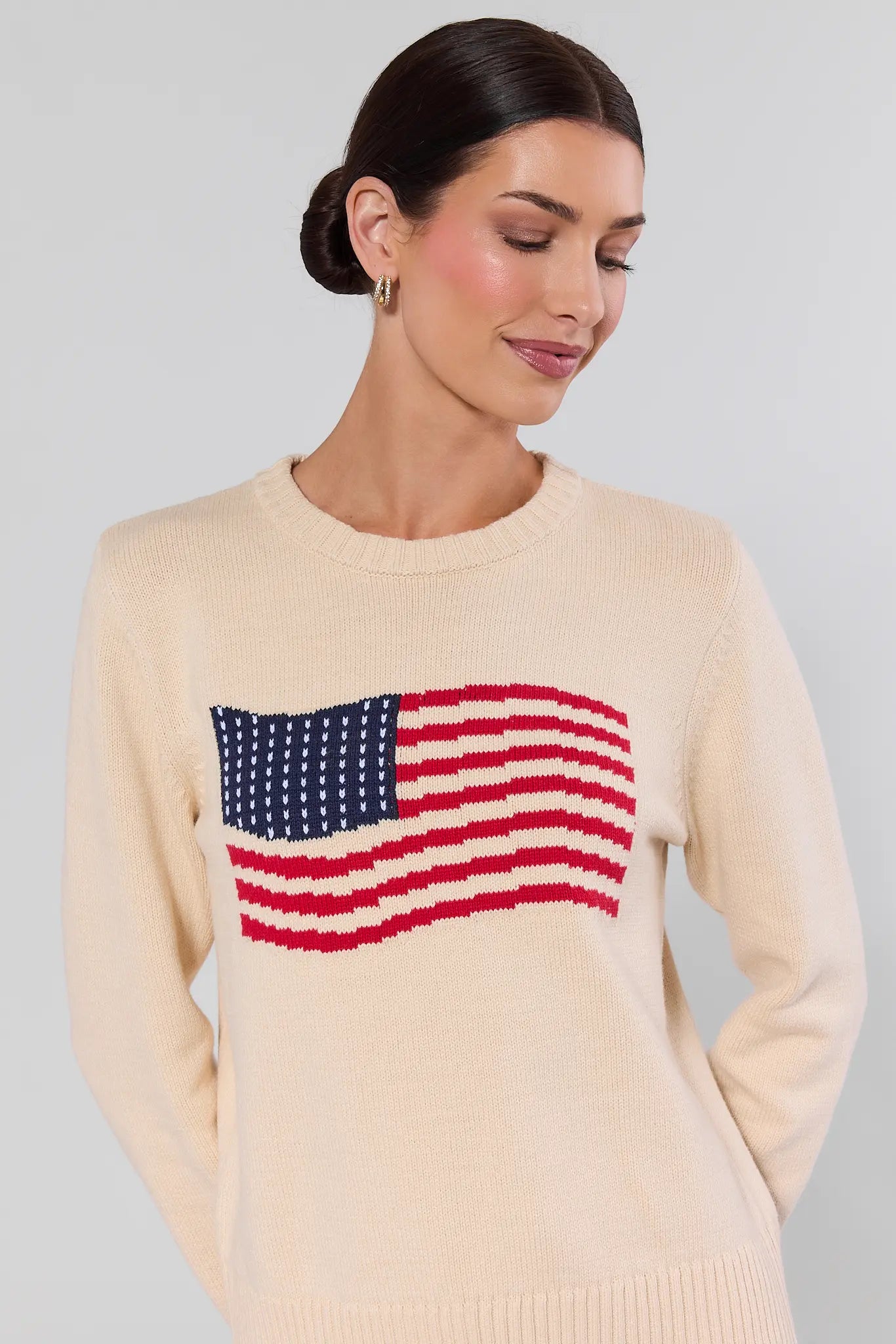 close up Woman wearing a cream sweater with an American flag design on a plain background