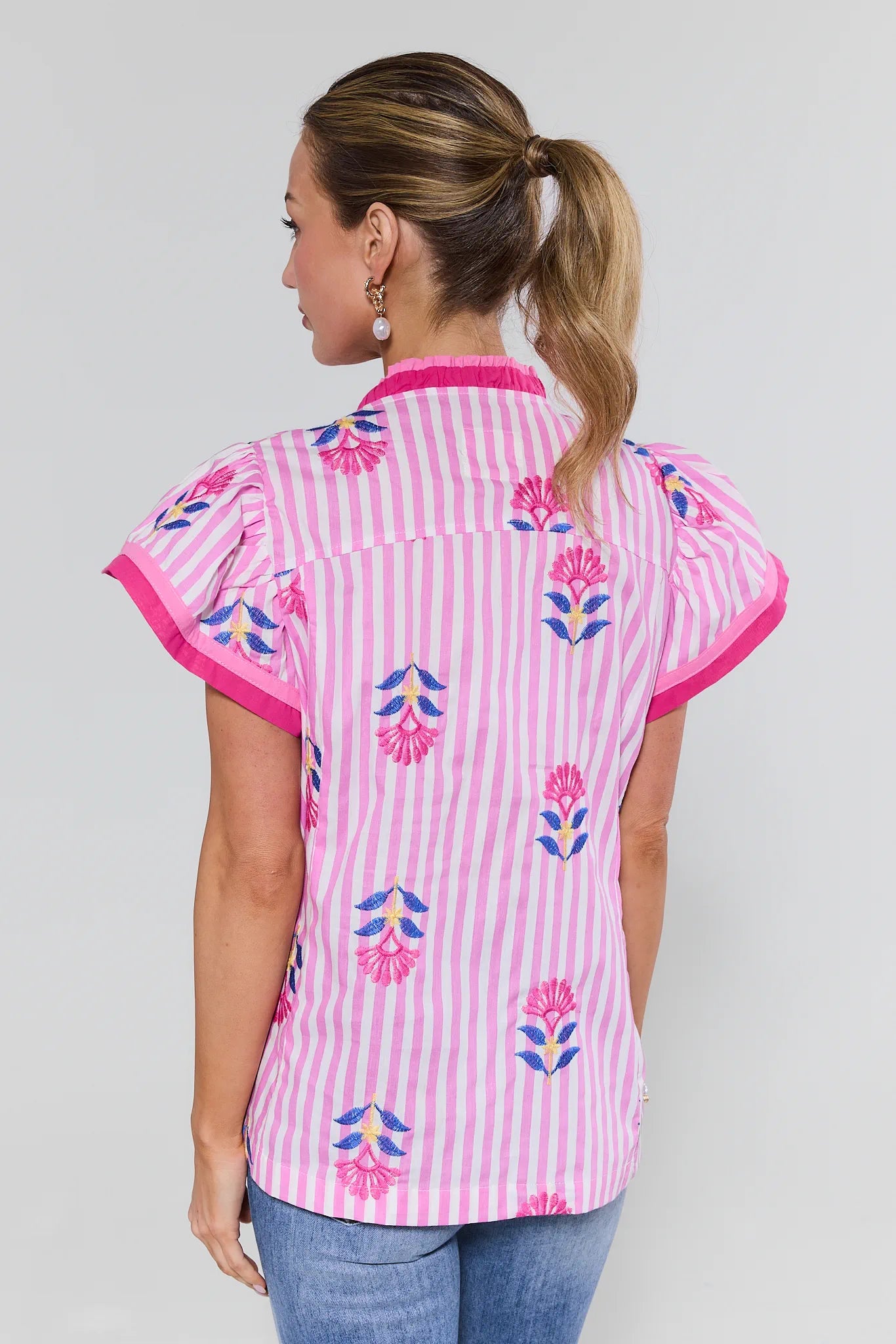 Woman wearing a pink and white striped shirt with floral patterns on a plain background