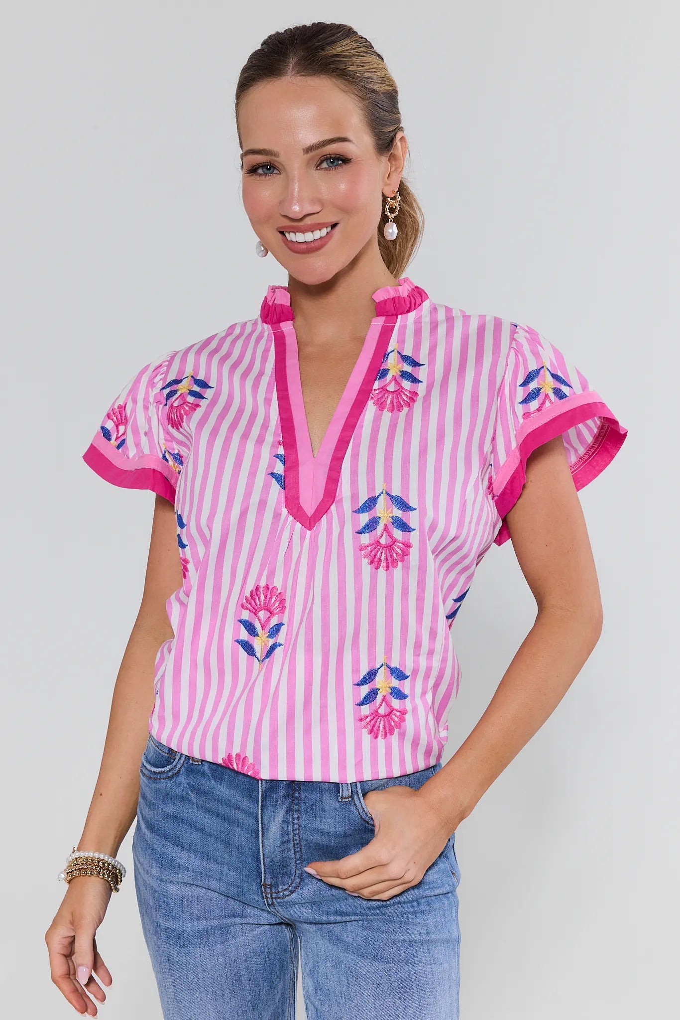 Woman wearing a pink and white striped top with floral embroidery on a plain background