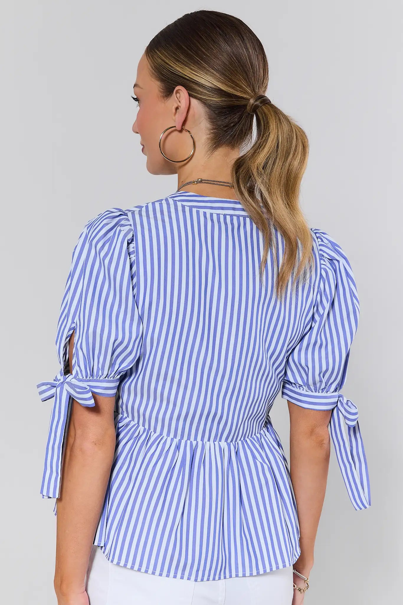 Woman standing wearing a blue and white striped blouse with tied sleeves on a plain background
