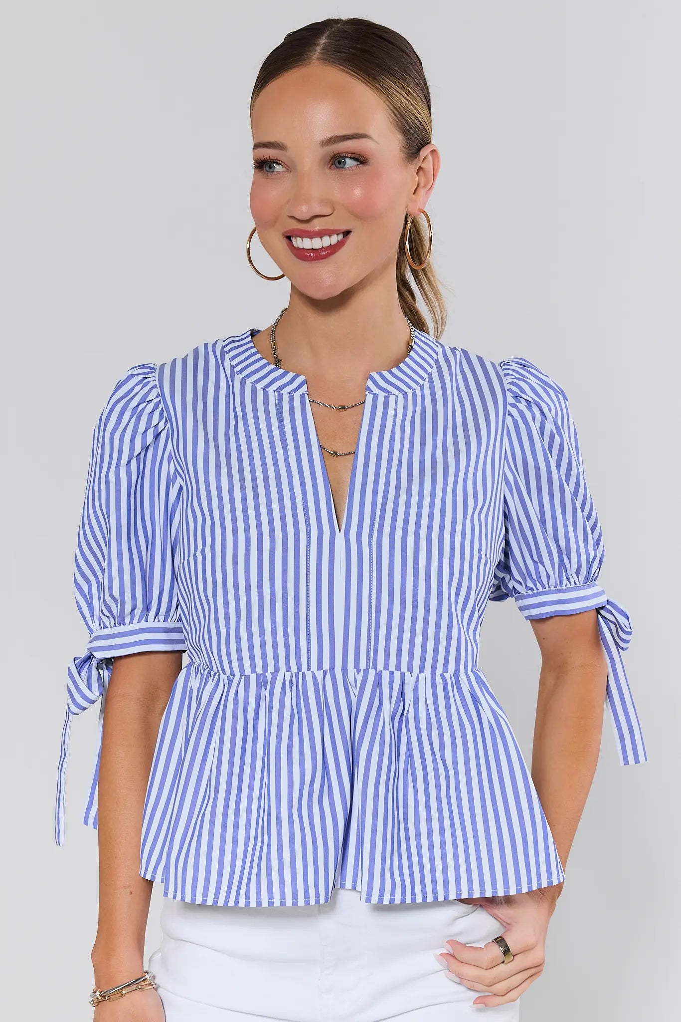 Woman wearing a blue and white striped blouse with tied sleeves on a plain background