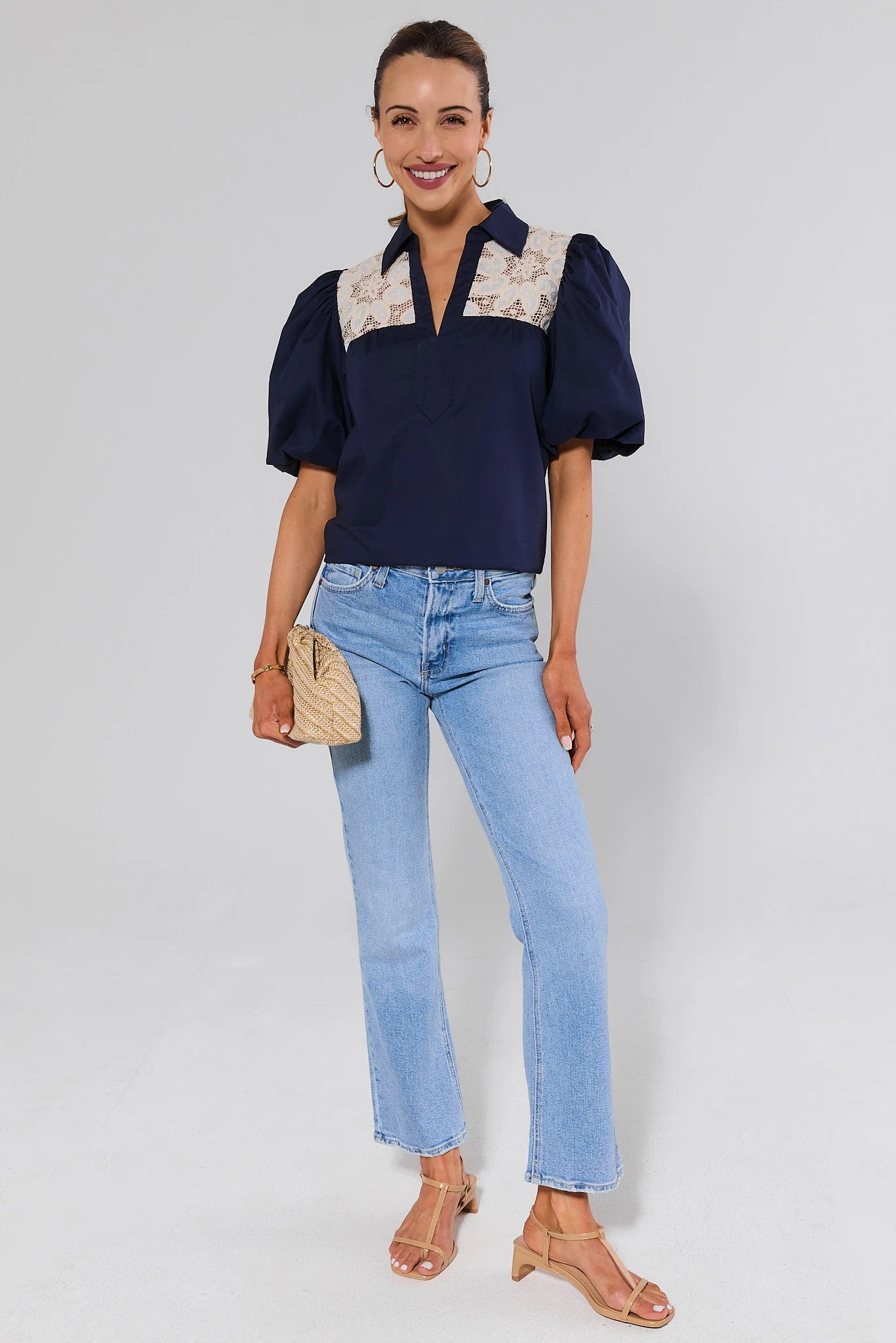 Woman wearing a navy blouse with floral collar and light blue jeans on a white background