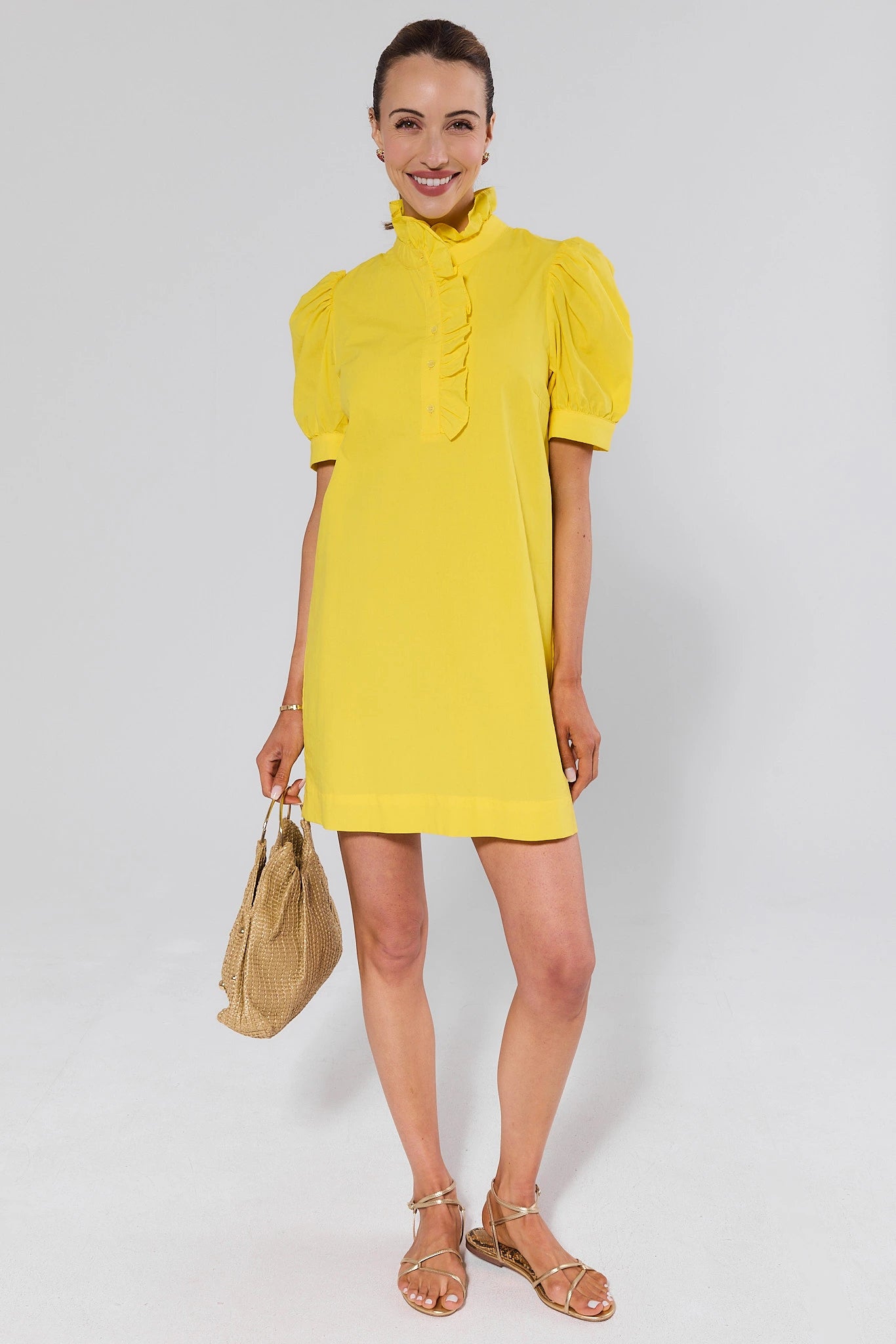 Woman wearing a yellow dress holding a beige handbag on a white background