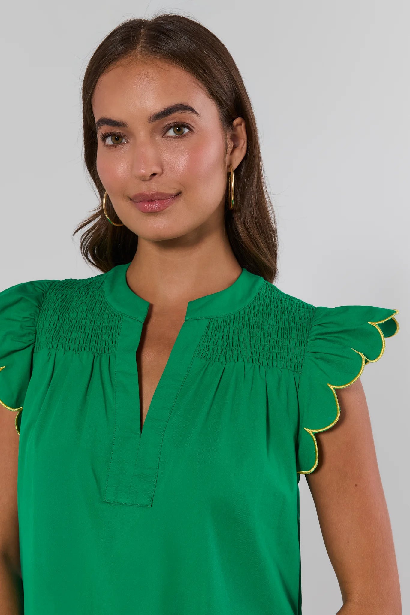 Woman wearing a green blouse with ruffled shoulders against a plain background close up